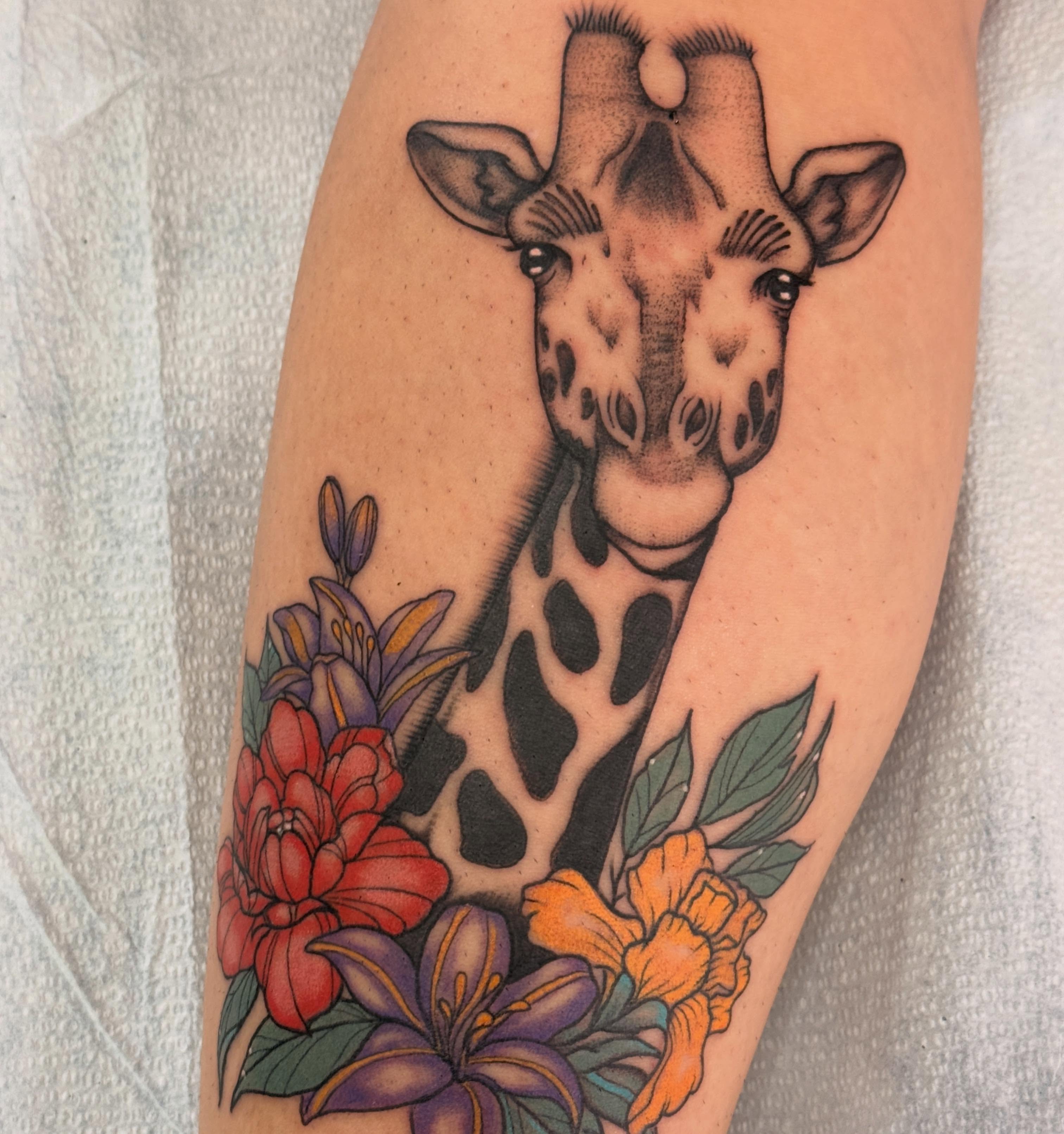 Giraffe with flowers realism tattoo on the forearm by Megan Sue Causemaker