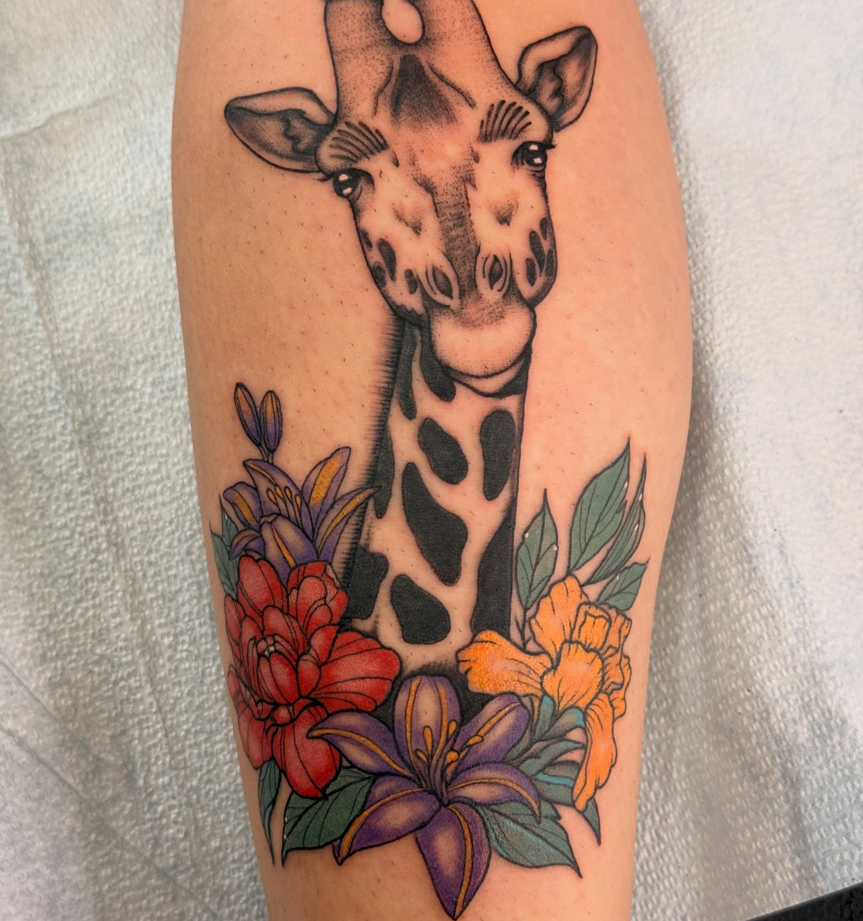 Giraffe with flowers realism tattoo on the forearm by Megan Sue Causemaker