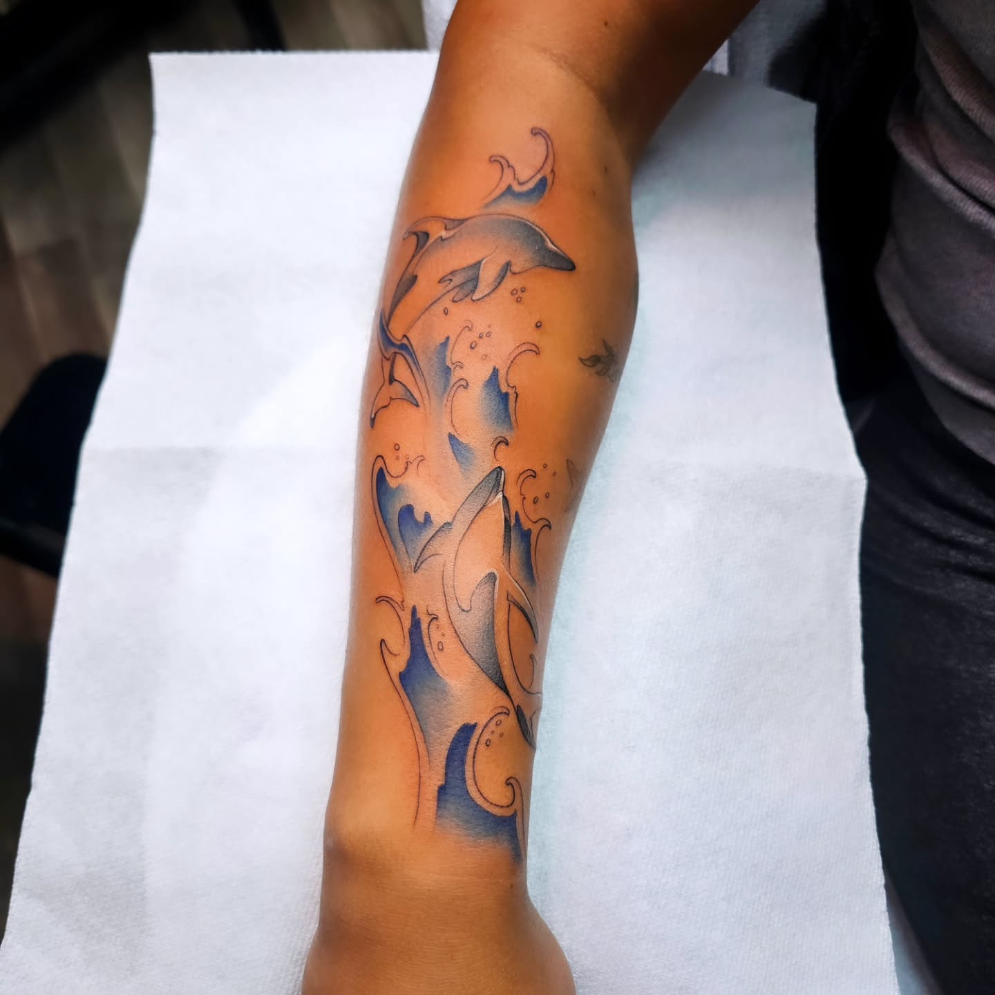 Dolphins and waves new school tattoo on the forearm by Adriannah Esparza