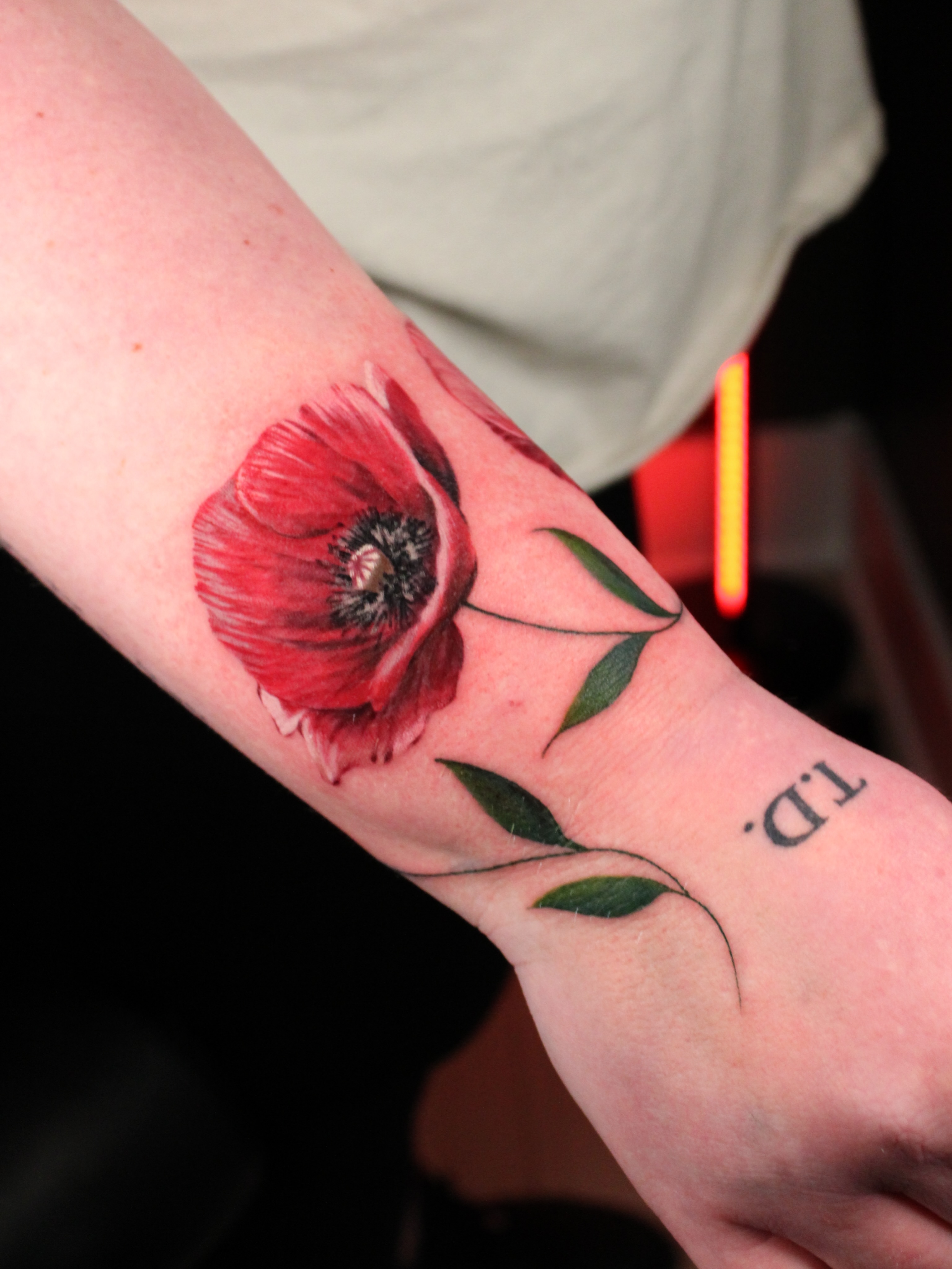 Red poppy realism tattoo on the forearm by Eva Williams