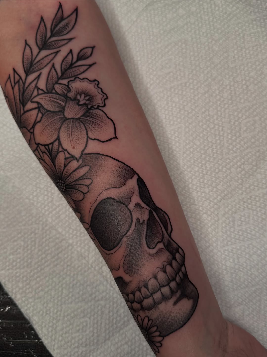 Skull with flowers realism tattoo on the forearm by Lisa Nikolopoulos, New York, New York