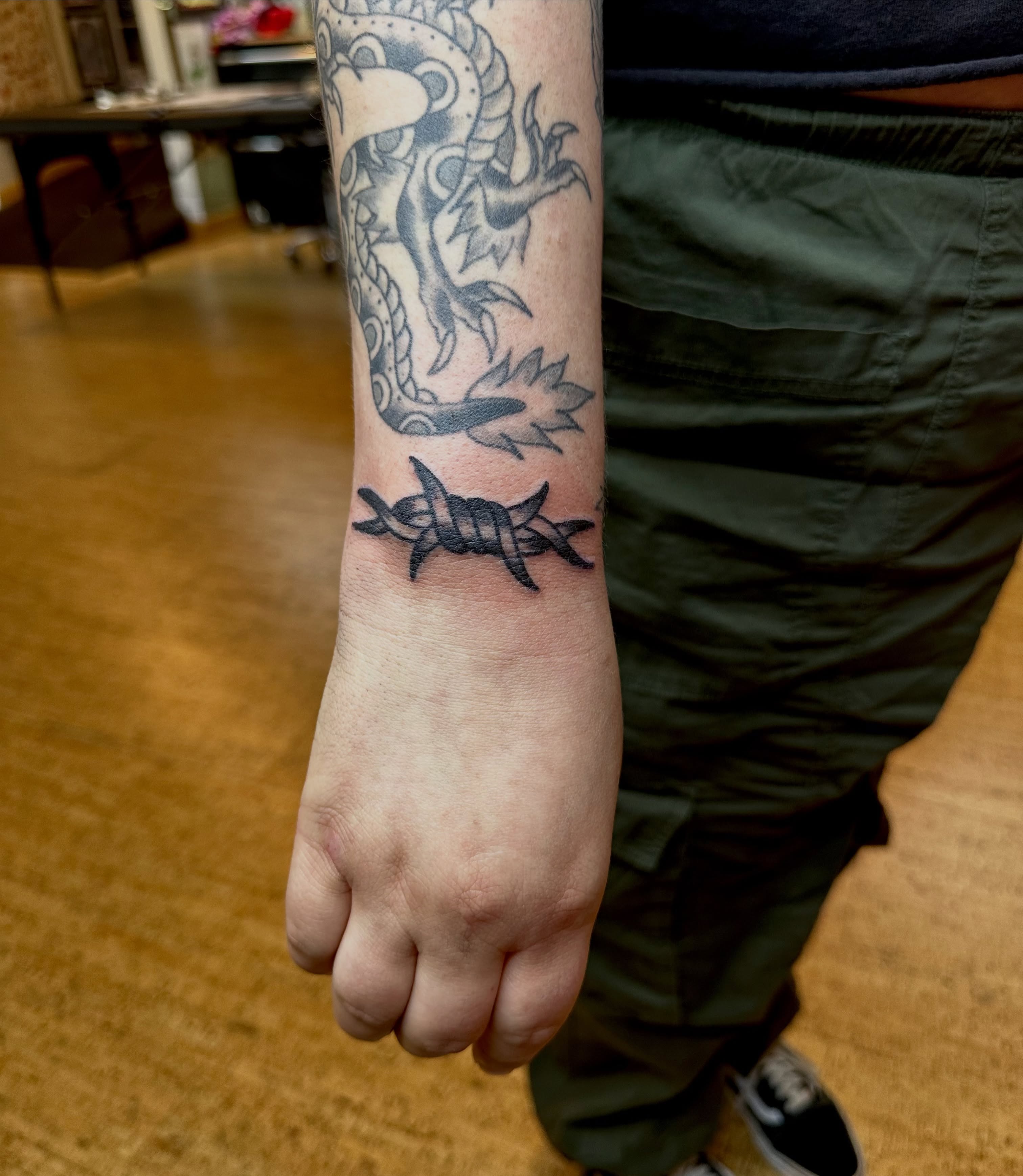 Dragon and barbed wire black and grey tattoo on the forearm by teddy, Portland, Oregon