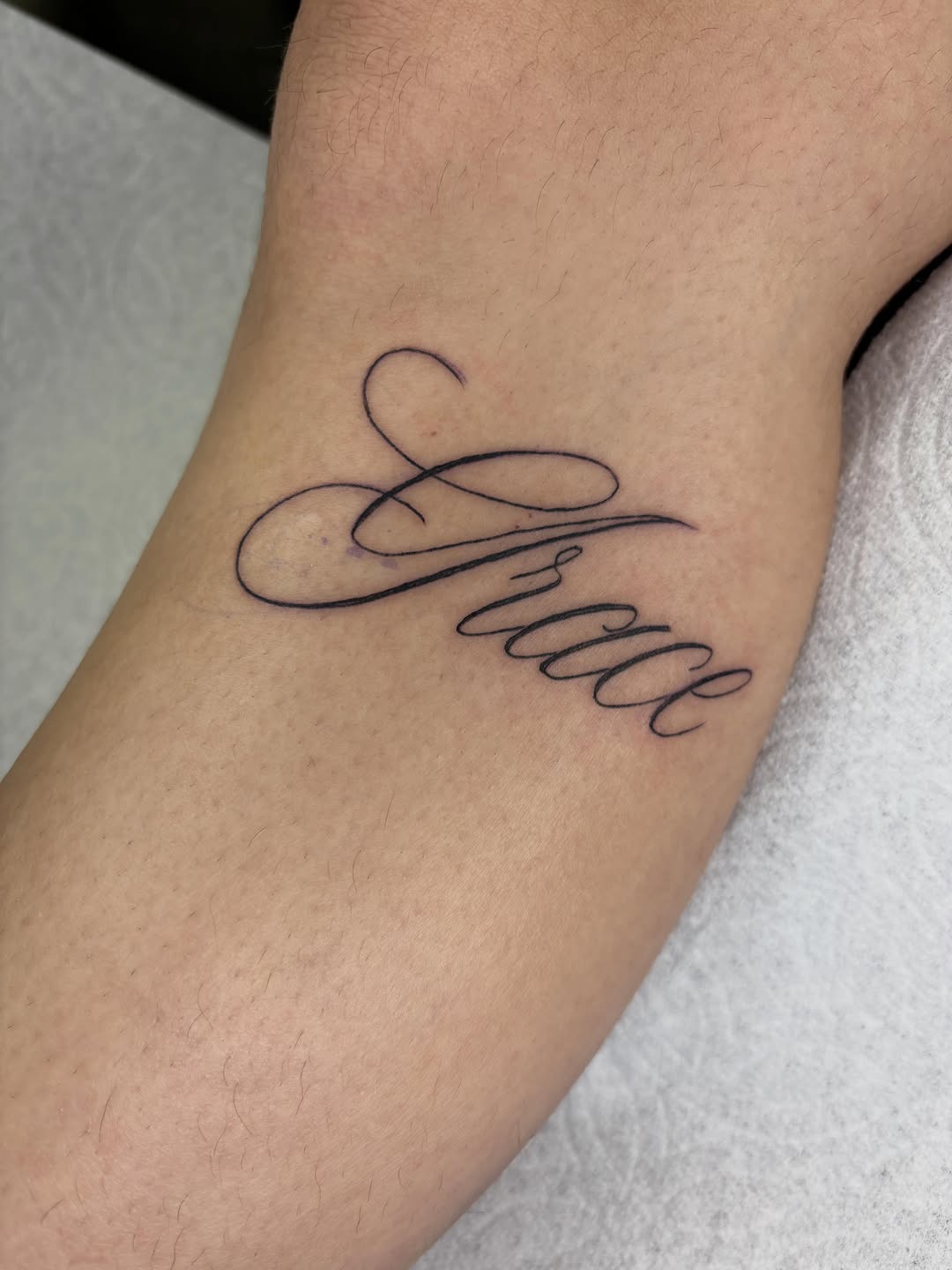 Script lettering 'Grace' lettering tattoo on the forearm by Amelia Rose, Los Angeles, California