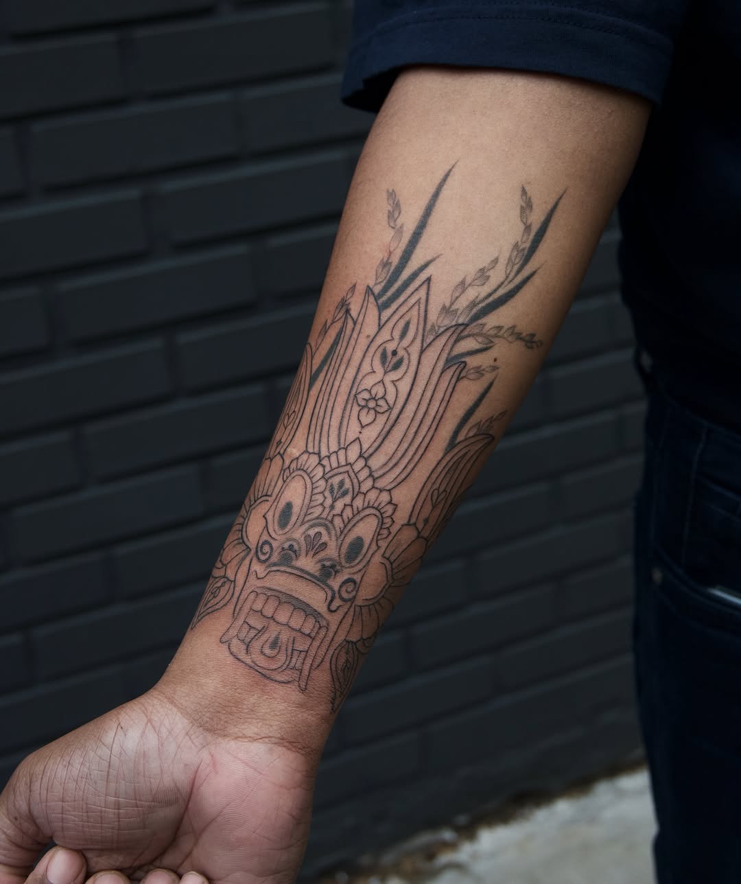 Mask black and grey tattoo on the forearm by Sabreena Haque