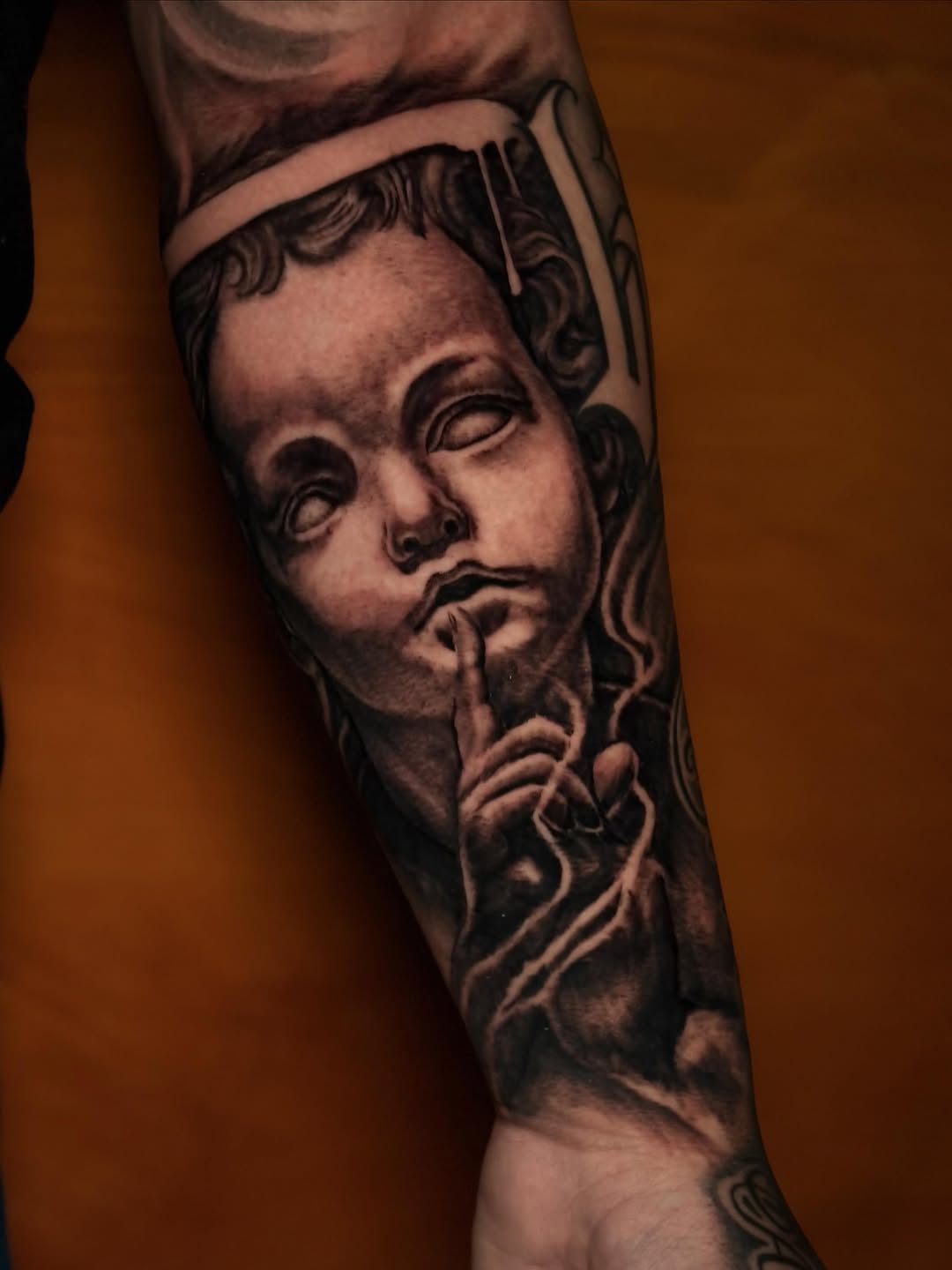 Cherub with finger to lips realism tattoo on the forearm by Trusty Dizon Tattoo Artist