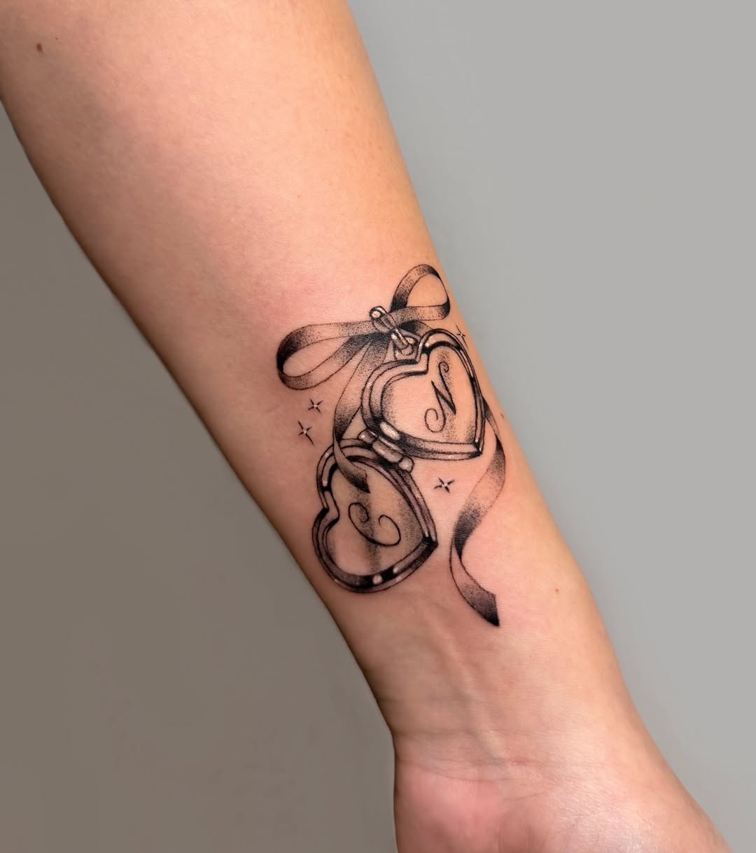Heart lockets with ribbon fine line tattoo on the forearm by Hery Anwar
