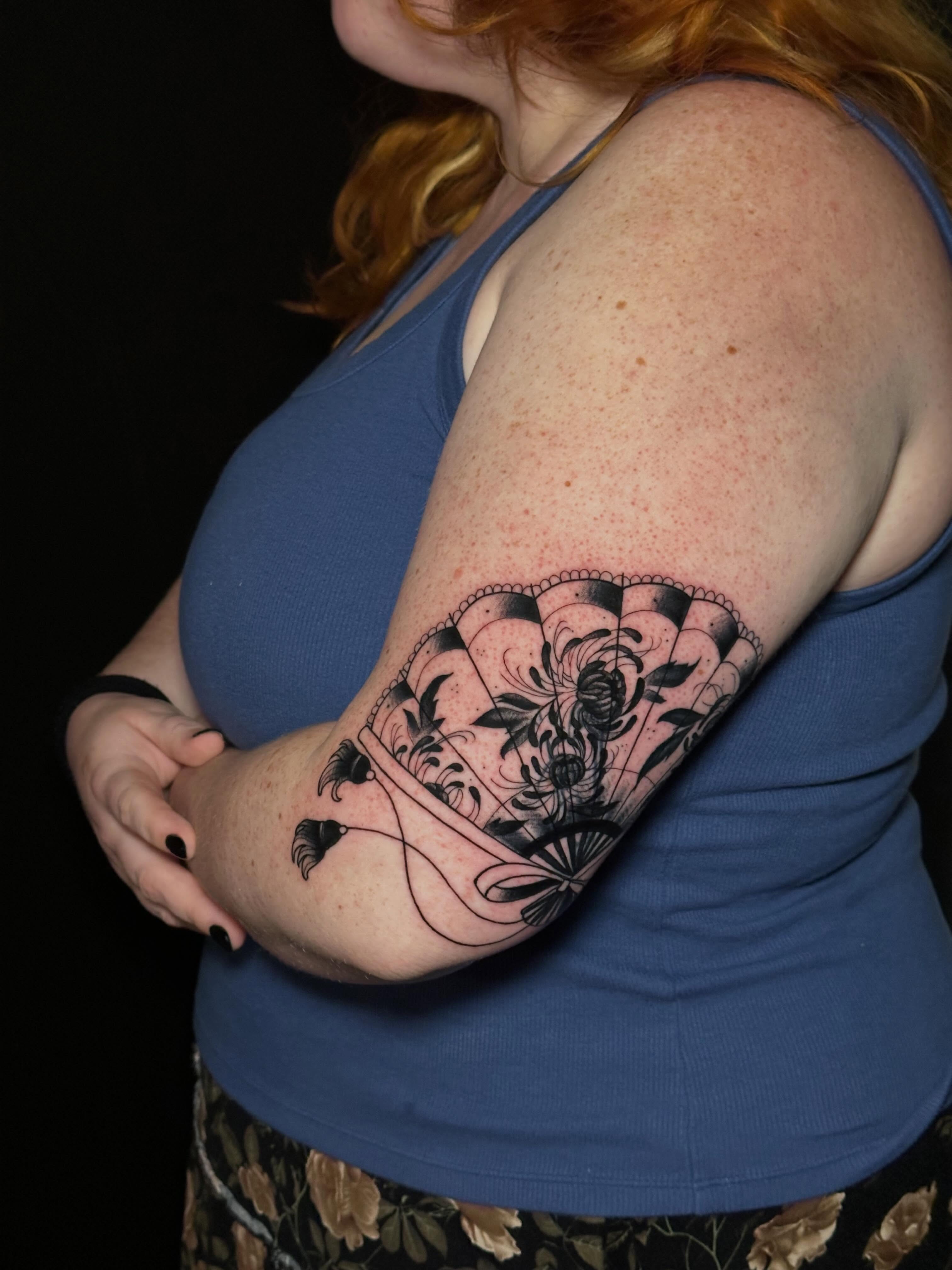 Fan with floral design black and grey tattoo on the upper arm by Liz McDonald