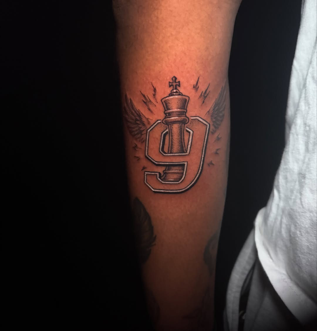 Number nine with chess piece black and grey tattoo on the forearm by Lauren B