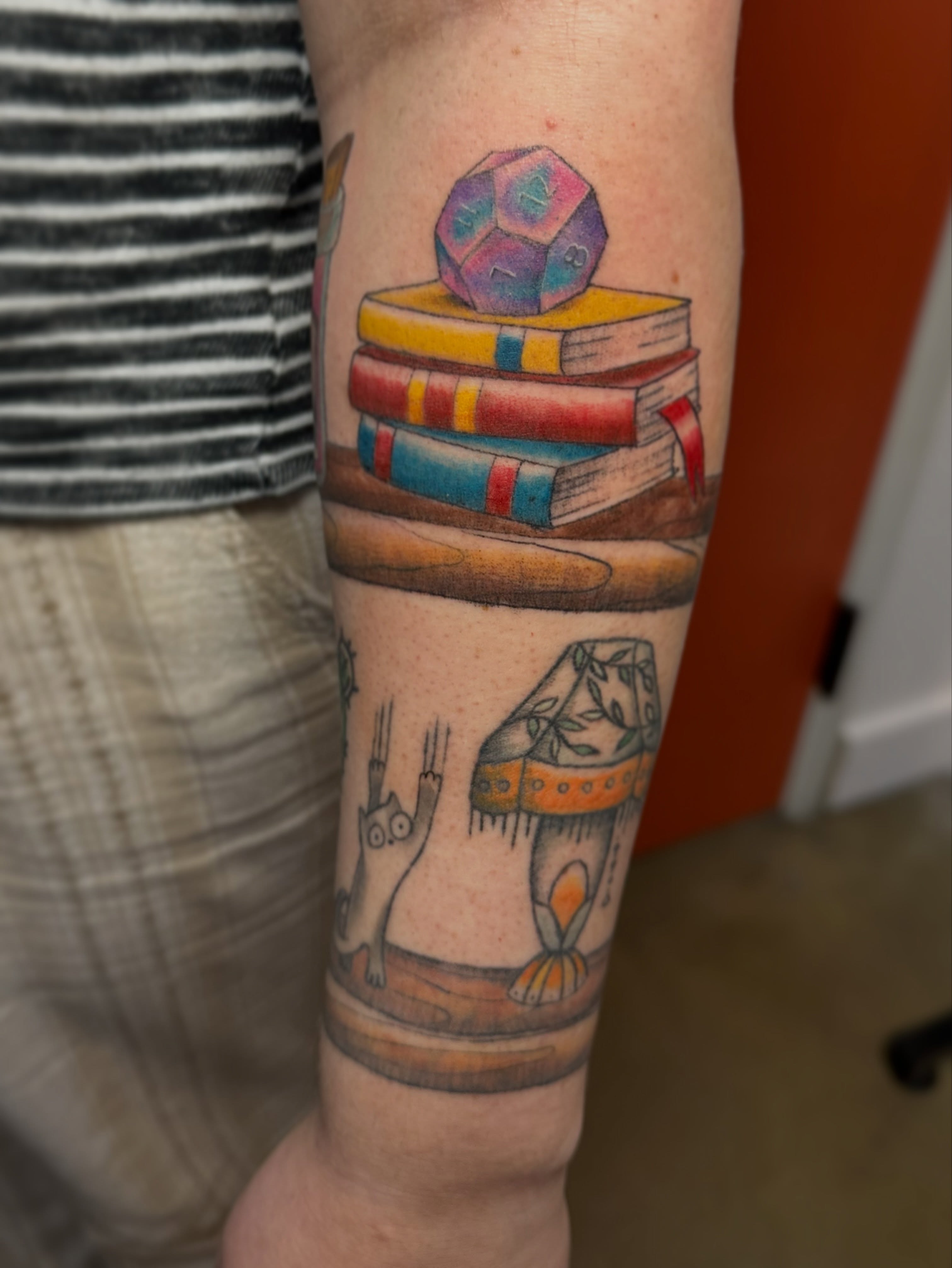 Books and dice new school tattoo on the forearm by Lauren DeLizza