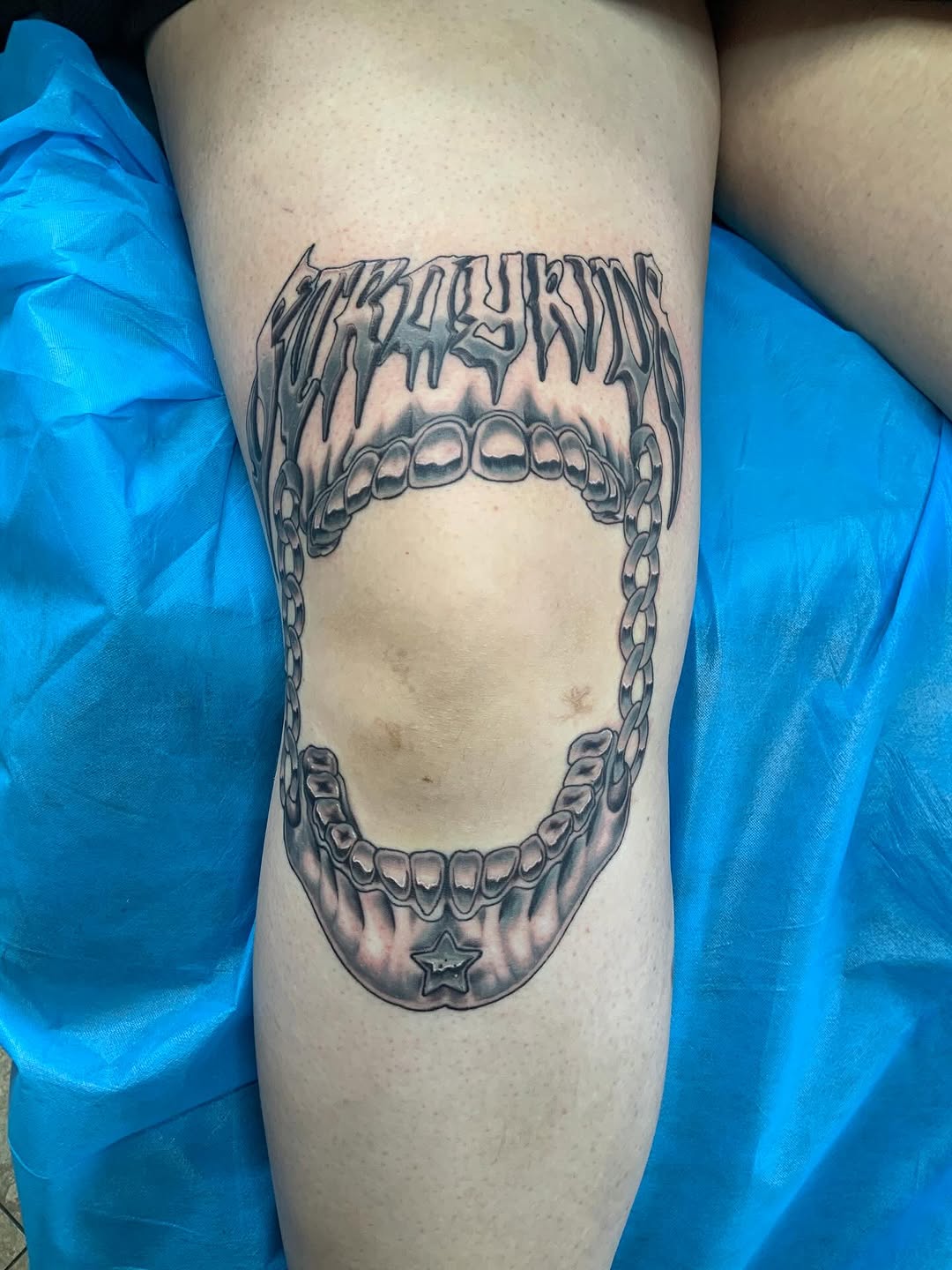 Jawbone with chain and lettering tattoo on the thigh by Anna Paulette