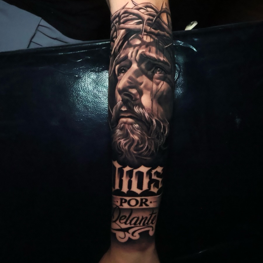 Jesus Christ portrait with lettering Chicano tattoo on the forearm by Angels tattoo