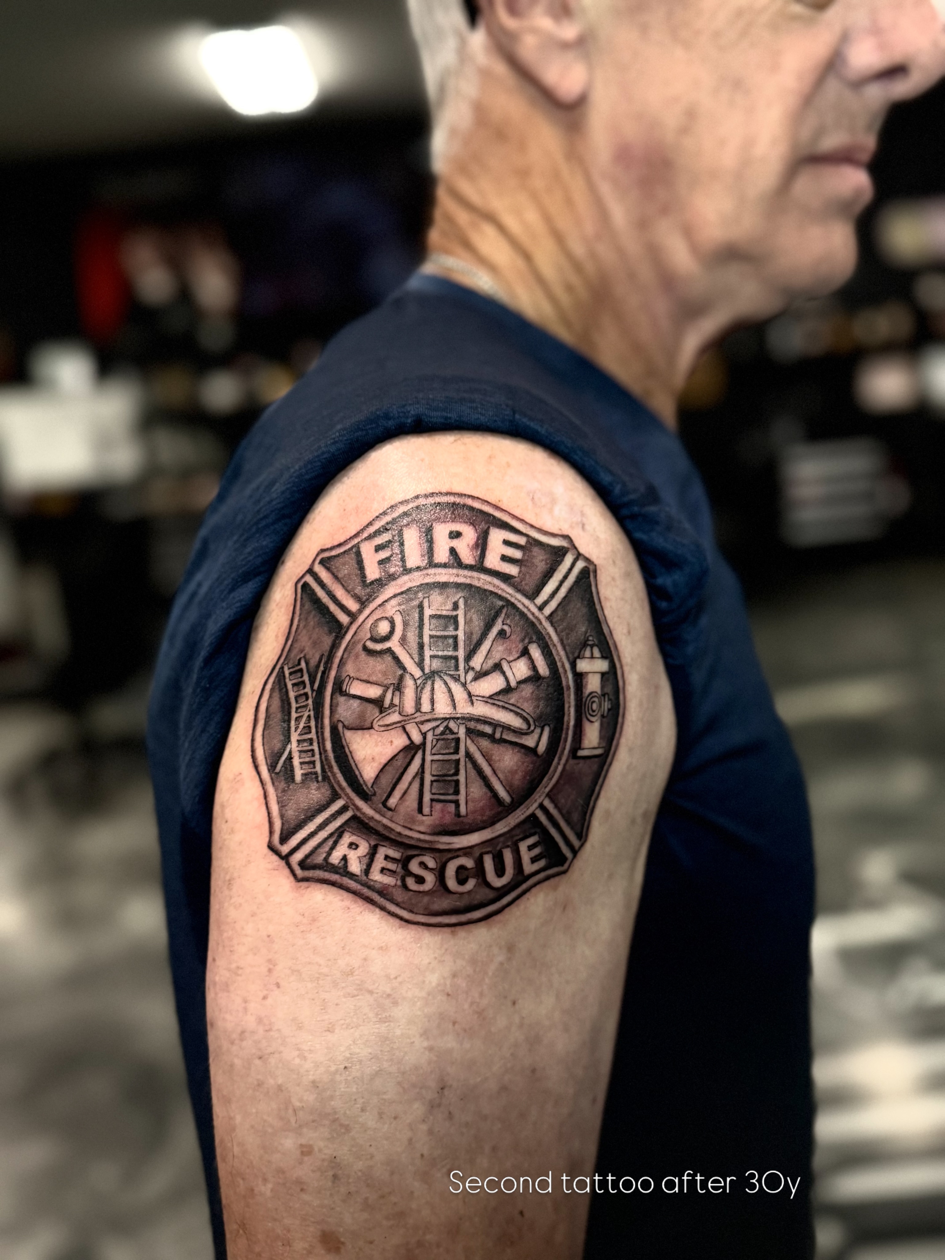 Fire rescue emblem black and grey tattoo on the shoulder by Paola Pineda Tattoo, Knoxville, Tennessee
