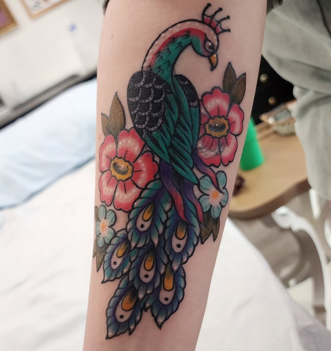 Peacock and flowers American traditional tattoo on the forearm by mikayla