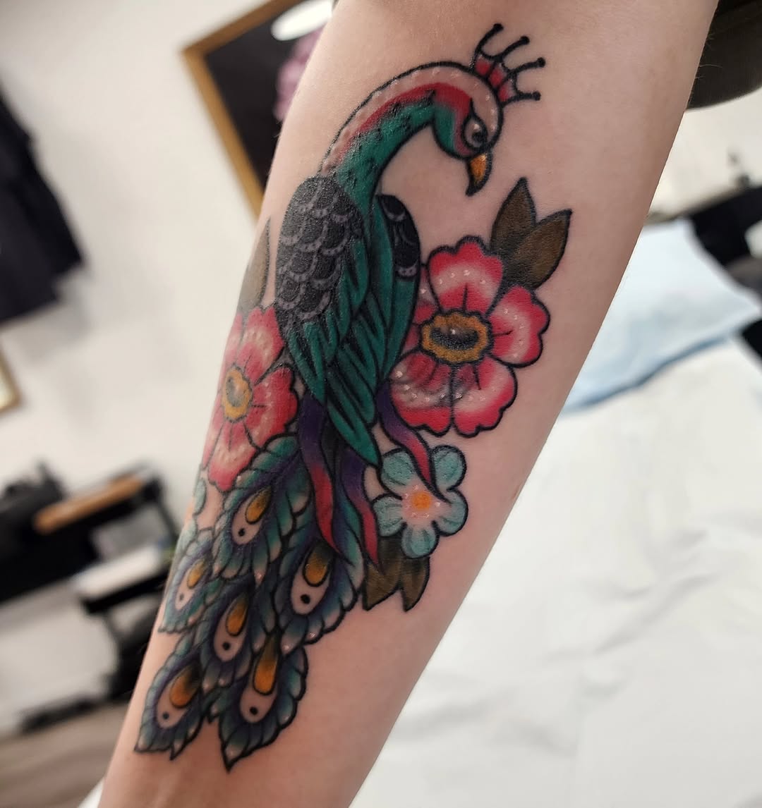 Peacock and flowers American traditional tattoo on the forearm by mikayla
