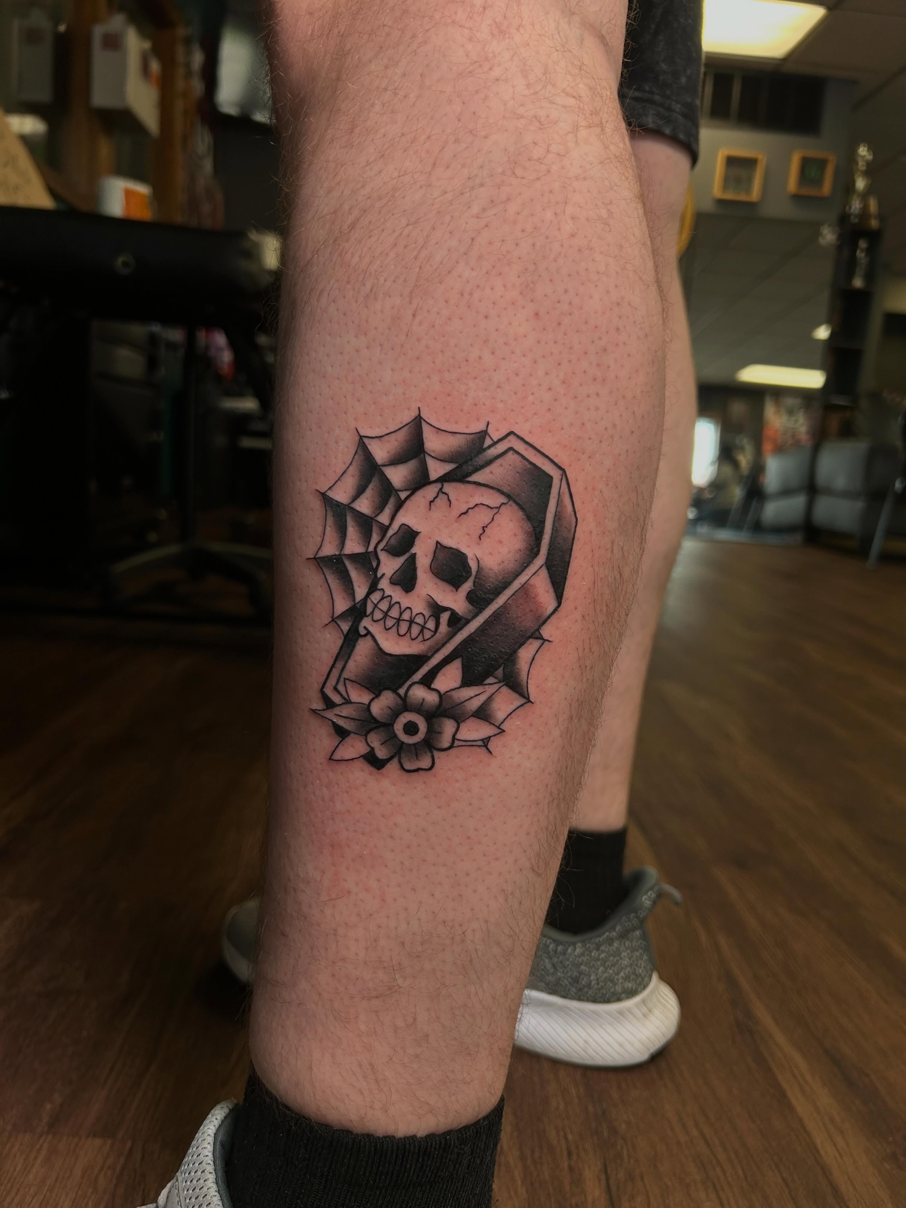Skull and flower black and grey tattoo on the calf by Vanessa Kendyll’s Tattoos