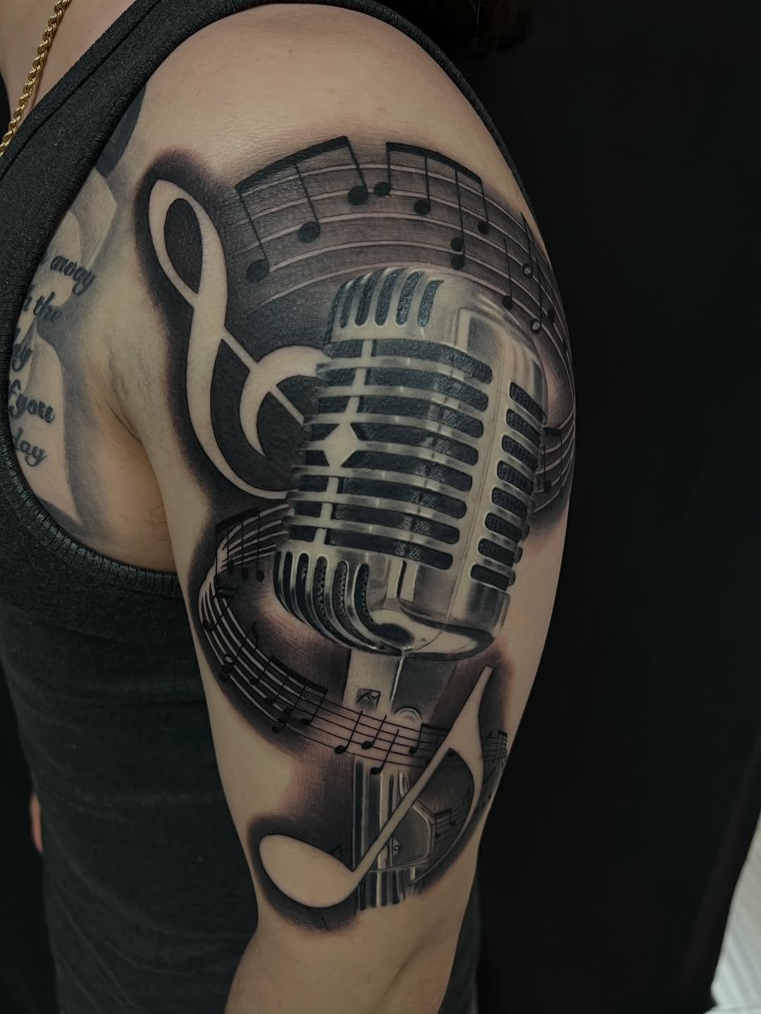 Vintage microphone with musical notes surrealism tattoo on the upper arm by Thomas Conard