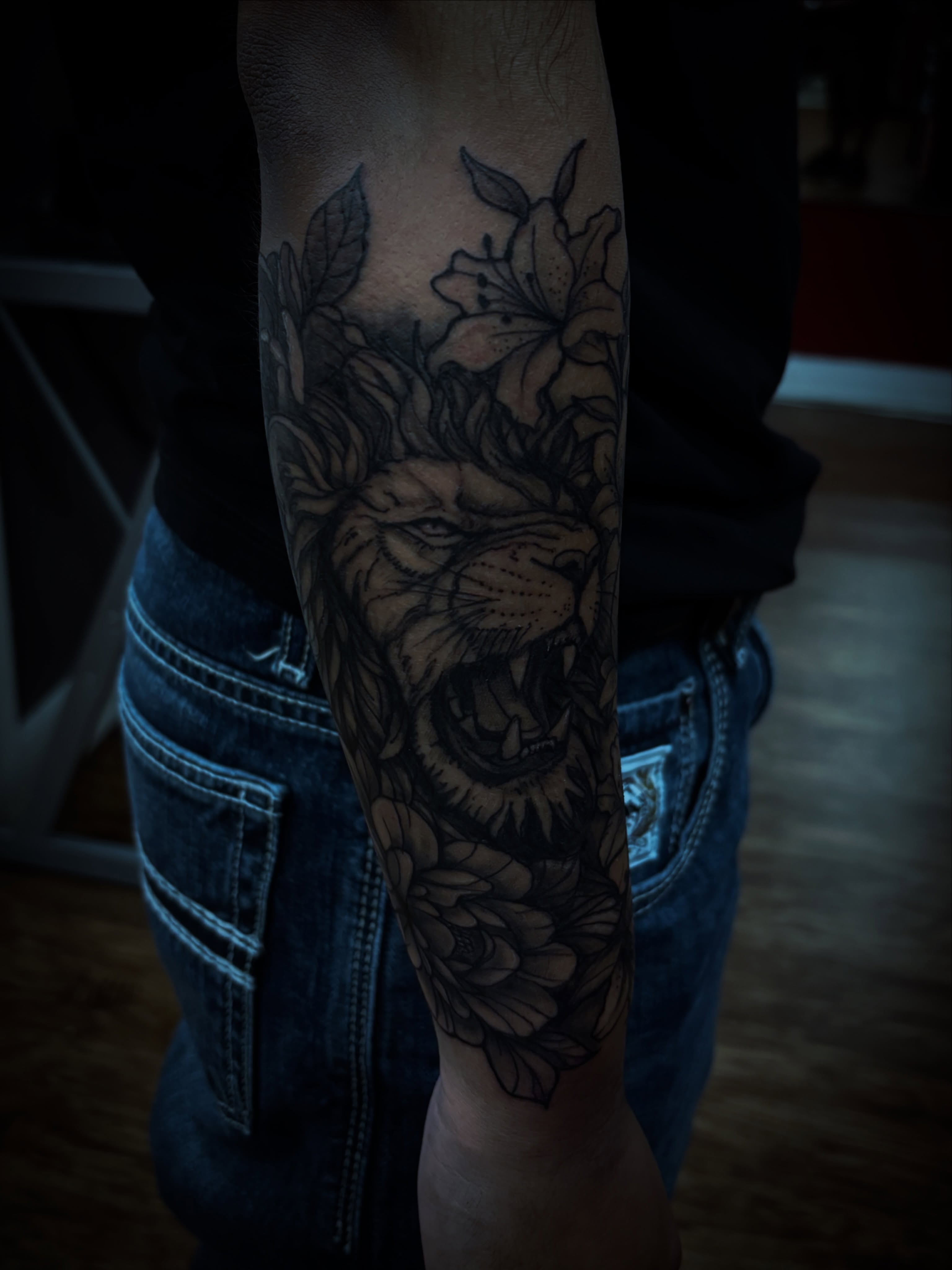 Lion with flowers black and grey tattoo on the forearm by Thom Johns-Green