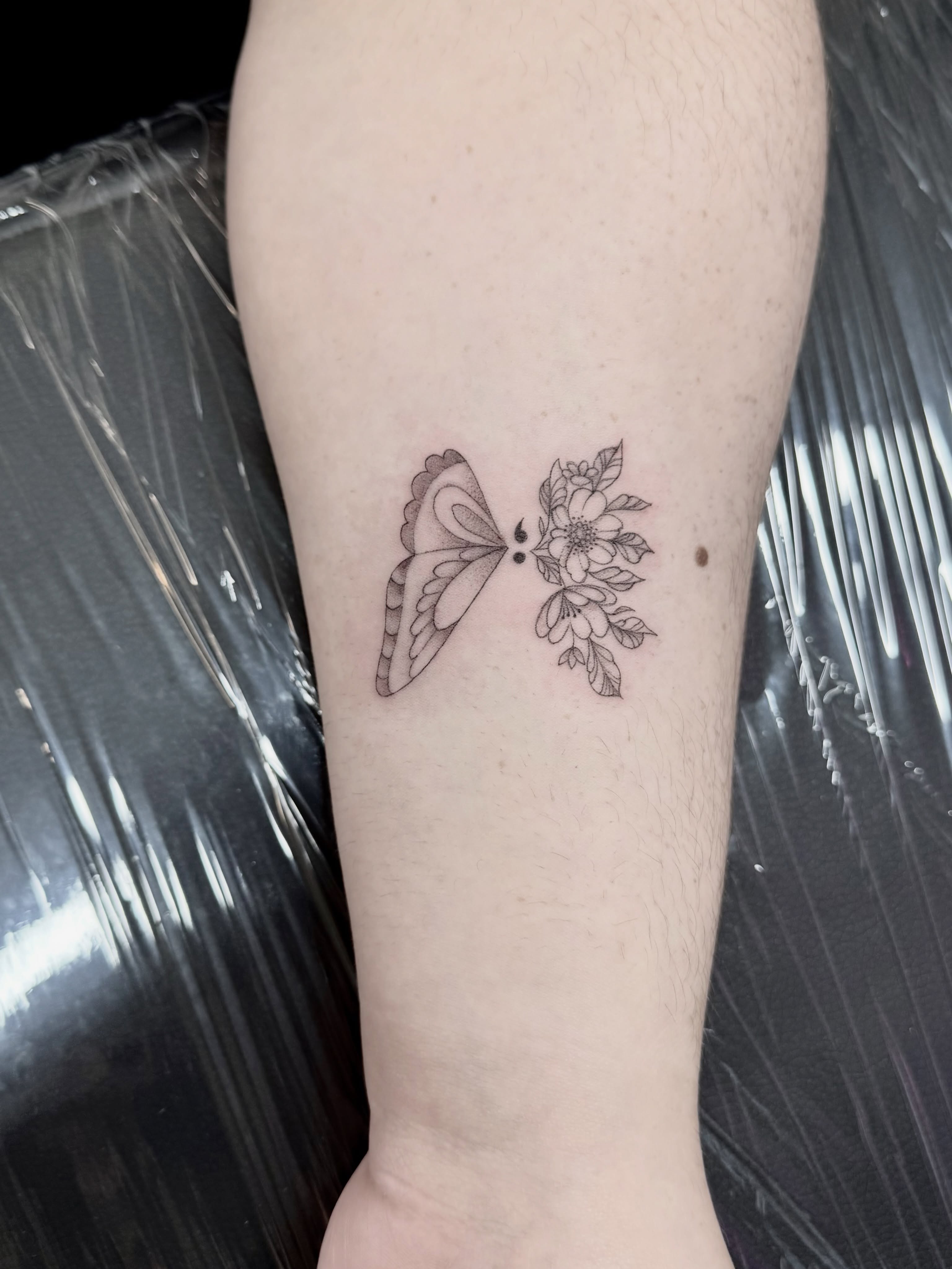 Butterfly and flower black and grey tattoo on the forearm by Anna