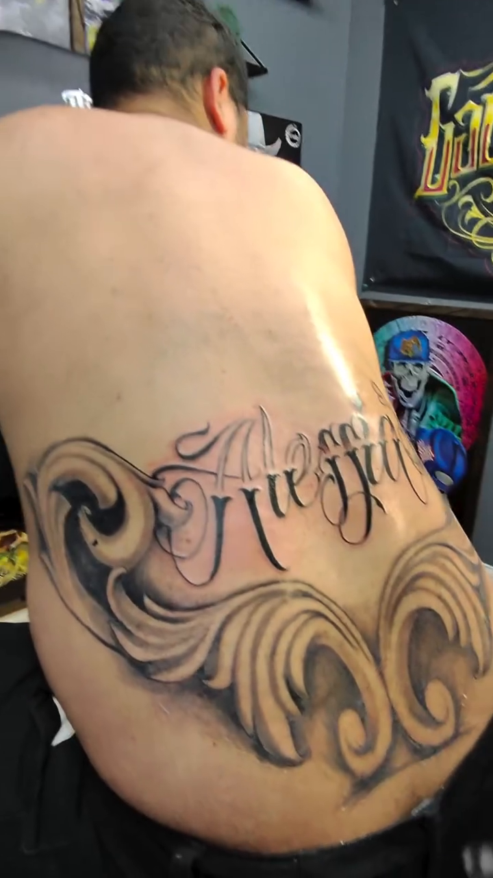 Alessia script with waves Chicano tattoo on the back by Oscar Saldaña