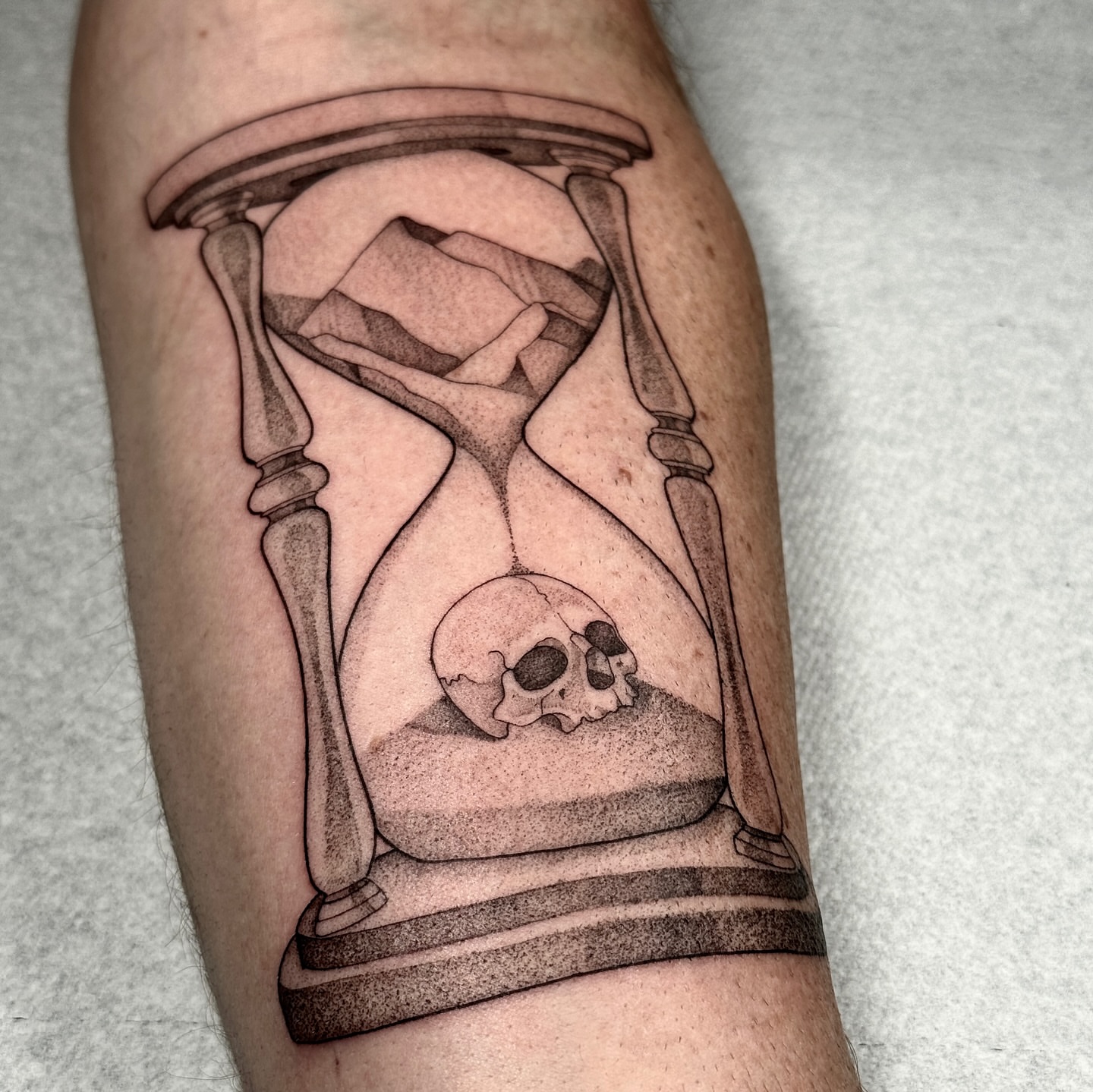 Hourglass with skull black and grey tattoo on the forearm by Molly Murray