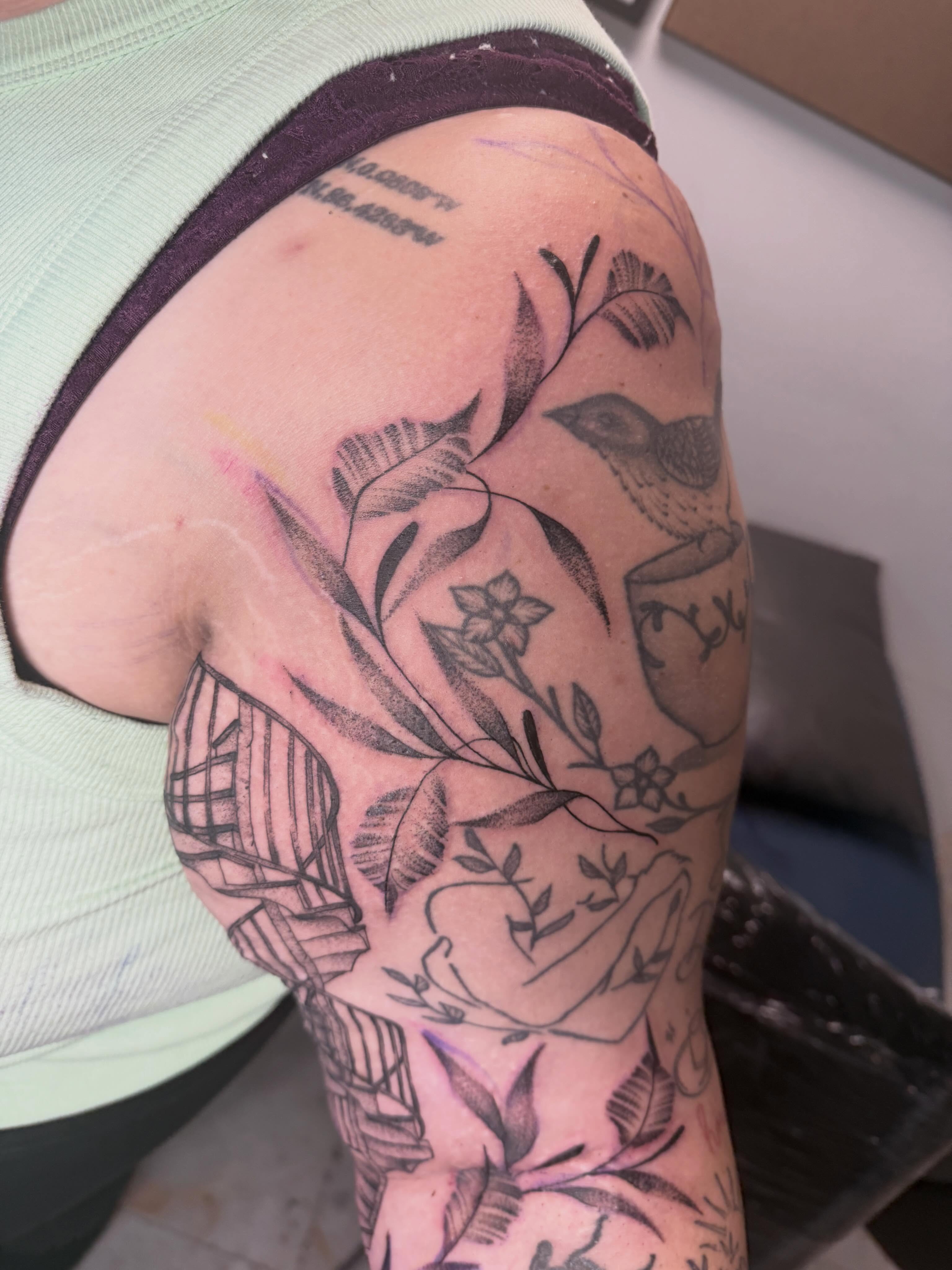 Botanical and bird black and grey tattoo on the upper arm by Abby