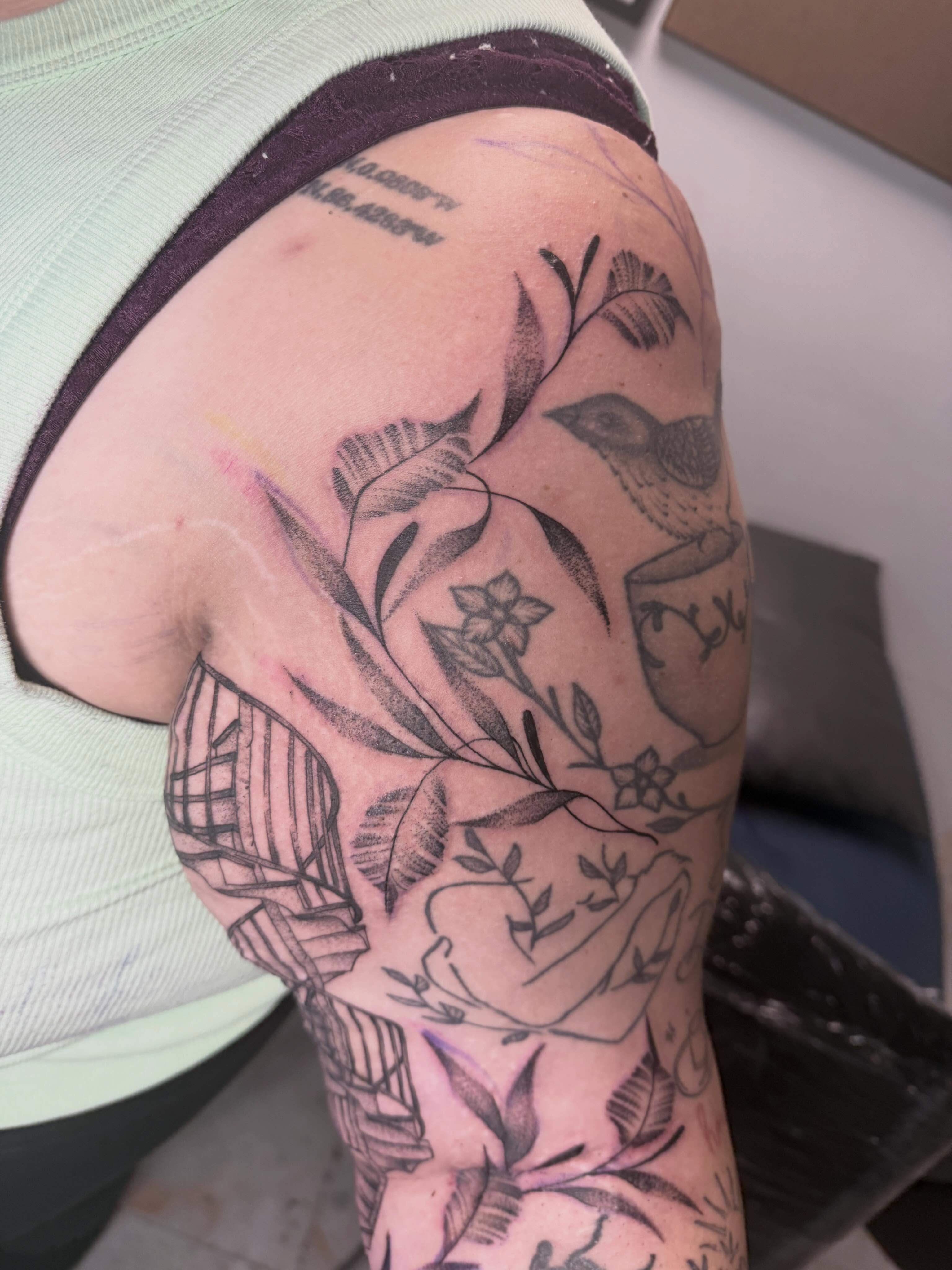 Bird and floral black and grey tattoo on the upper arm by Abby