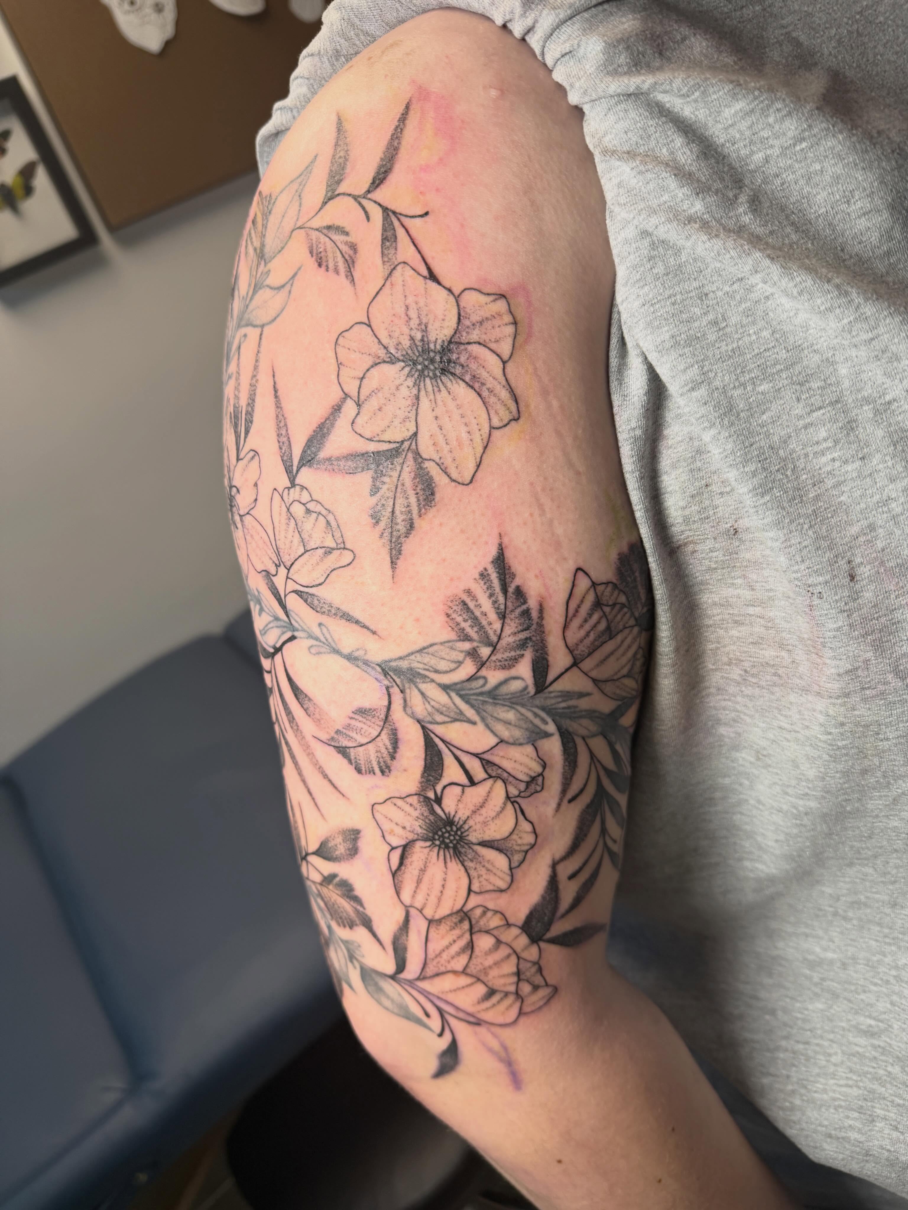 Floral arrangement black and grey tattoo on the upper arm by Abby