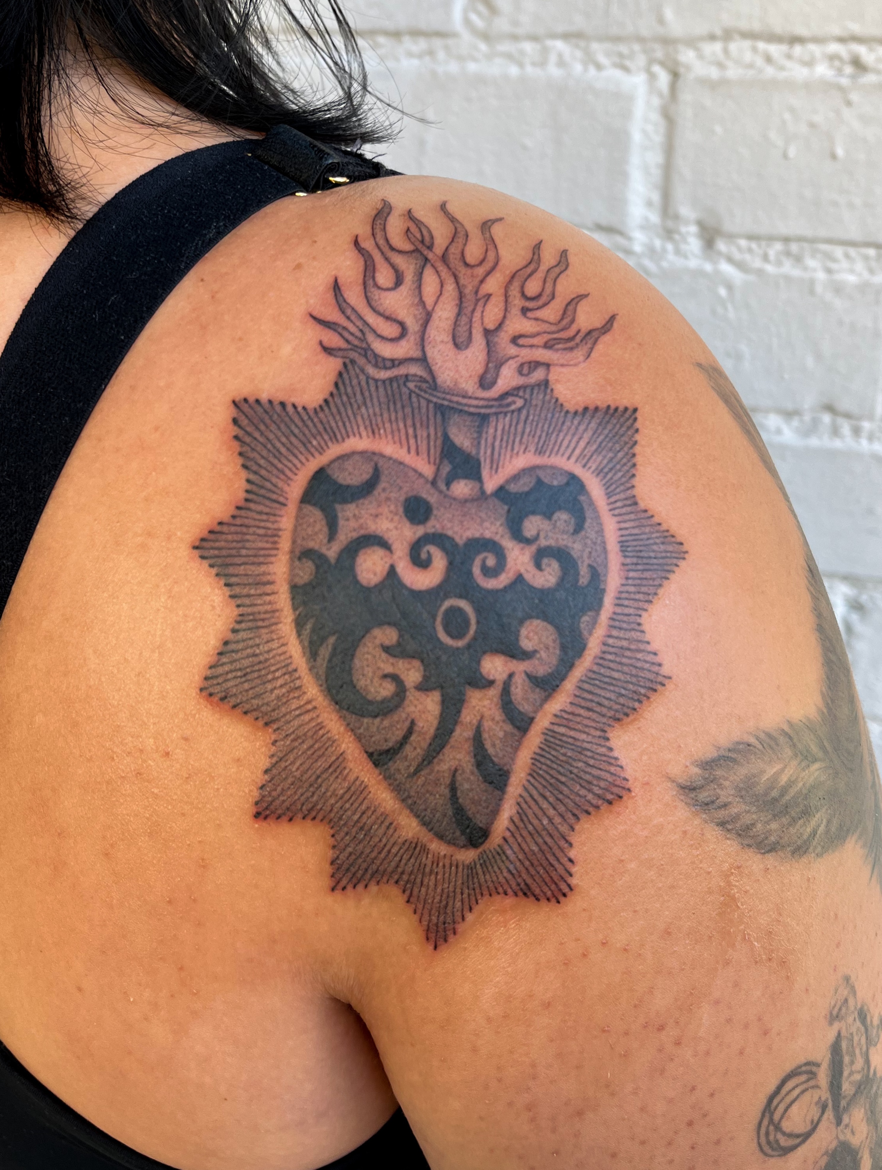 Heart with flames black and grey tattoo on the shoulder by The One Who’s Always Drawing