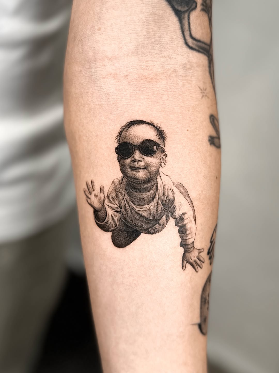 Baby wearing sunglasses crawling realism tattoo on the forearm by Saru