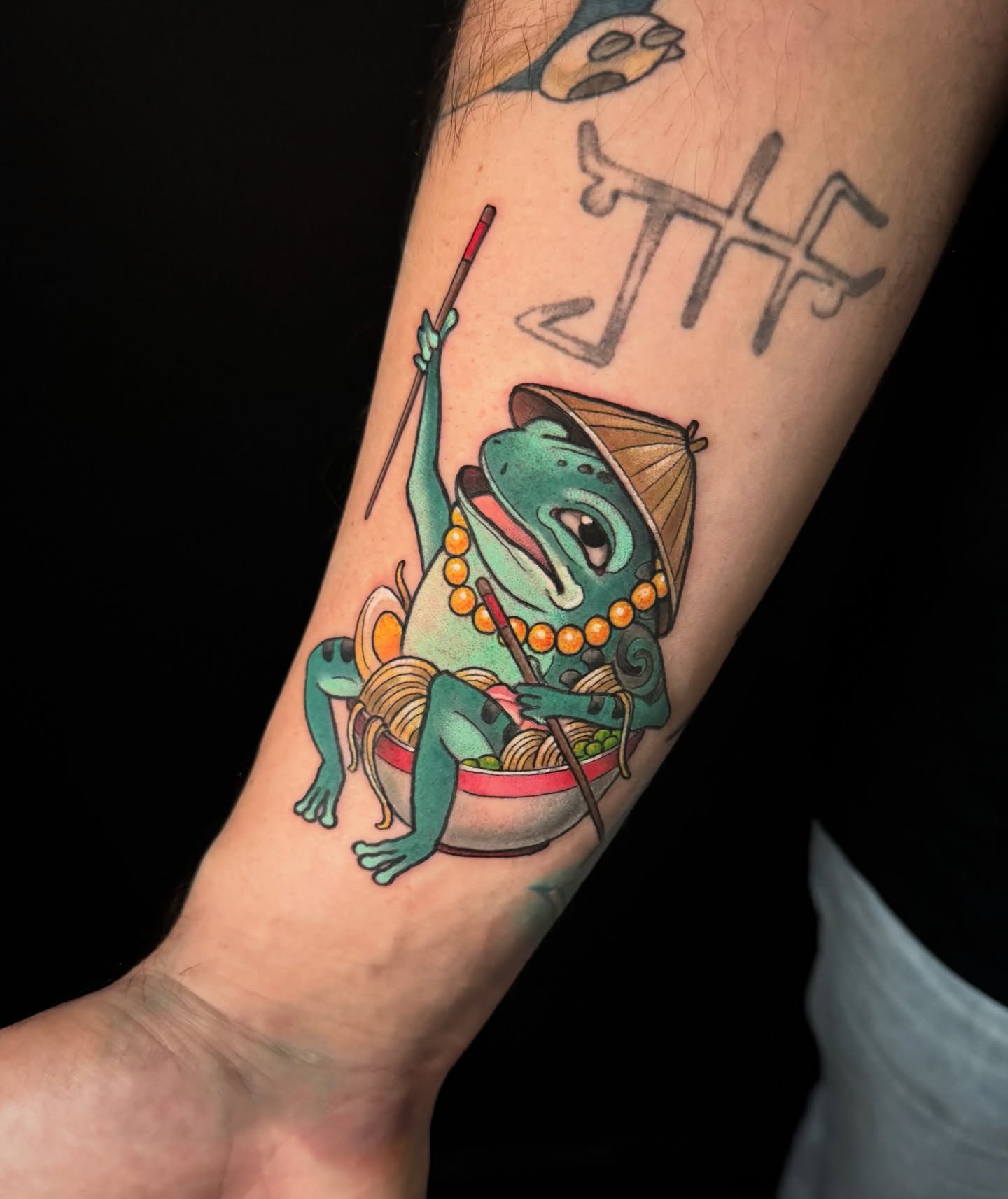Frog eating noodles new school tattoo on the forearm by Dee Florian