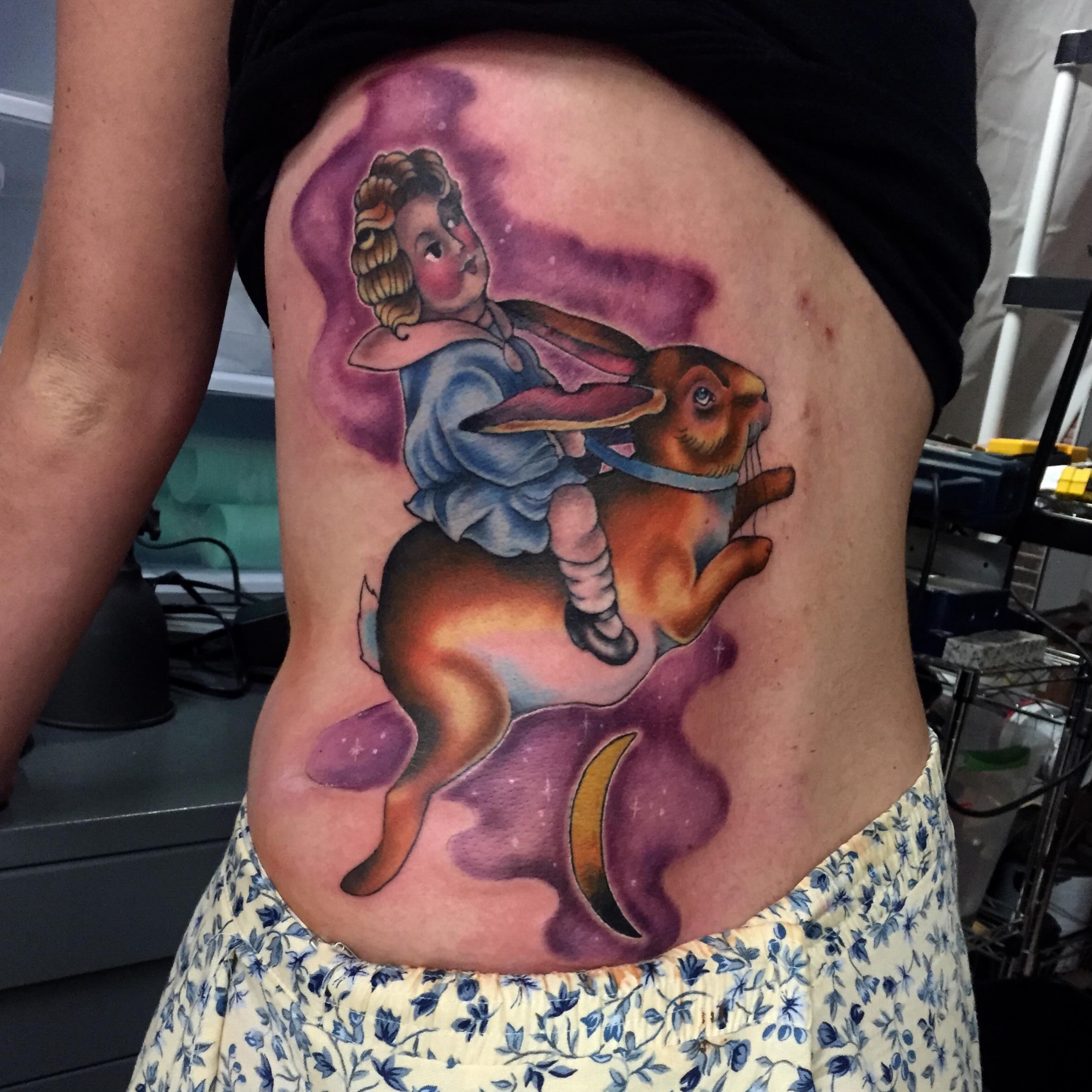 Girl riding rabbit illustrative tattoo on the ribs by Jamie Winn