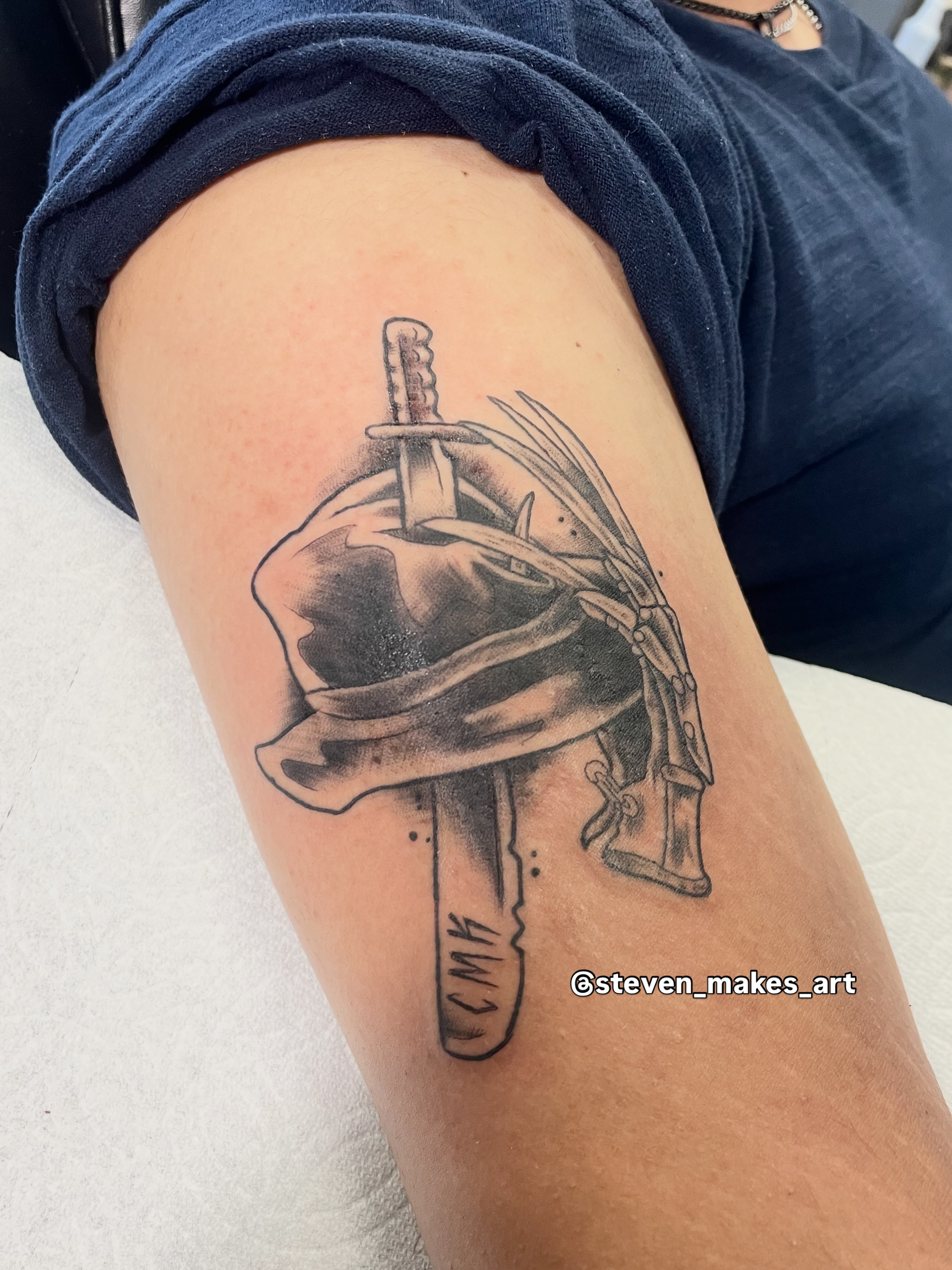 Helmet with sword black and grey tattoo on the thigh by Steven Hodges