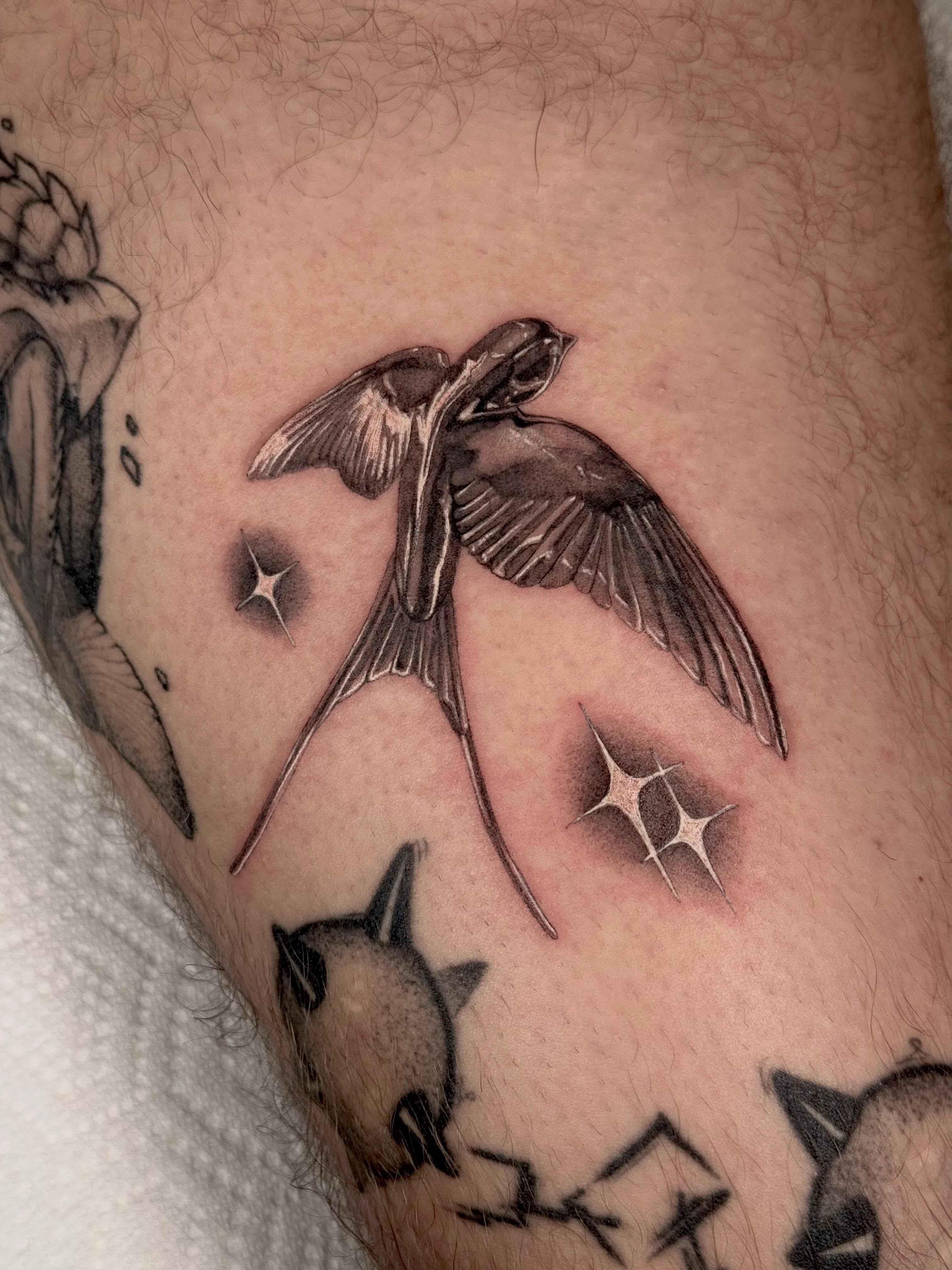 Swallow and stars black and grey tattoo on the forearm by Em Krieg