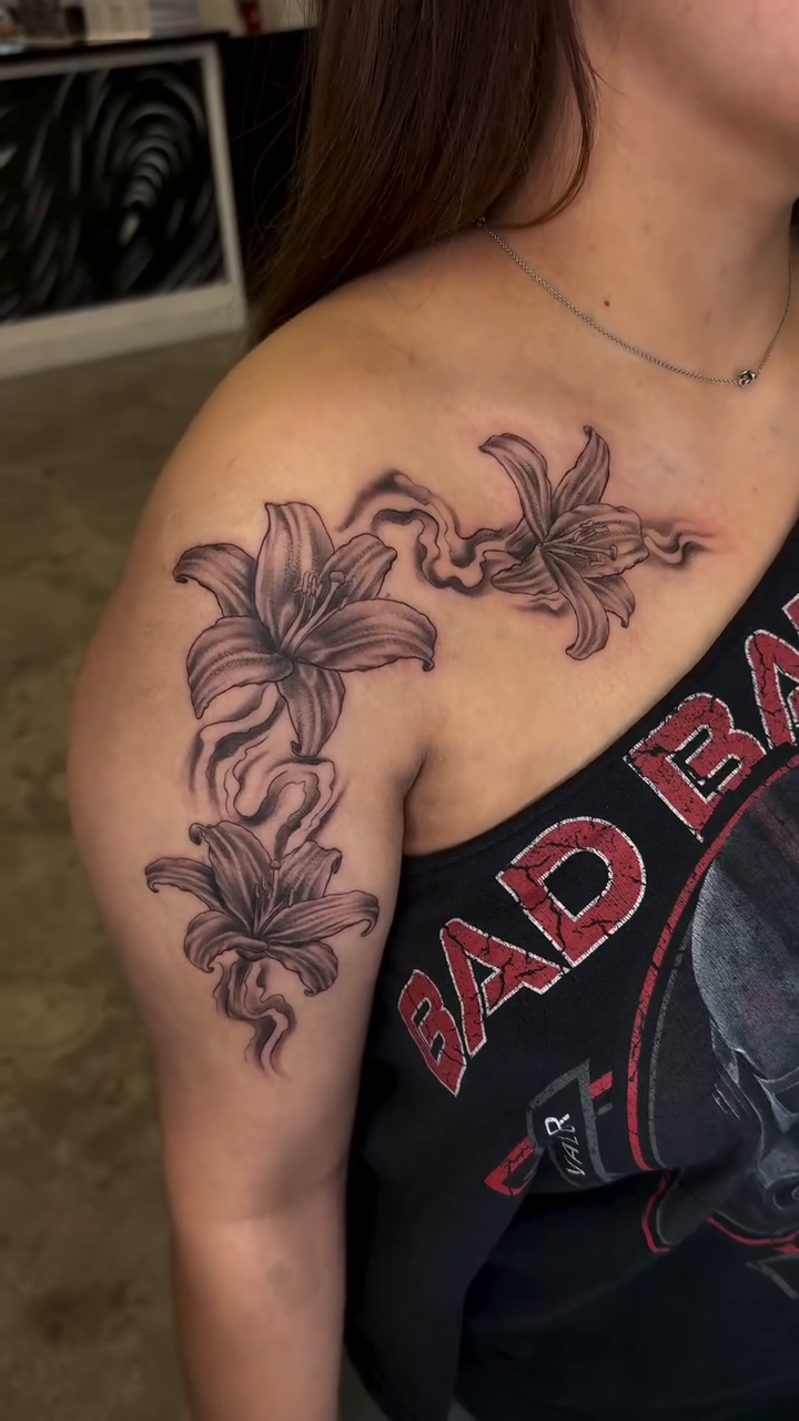 Lily flowers on shoulder and arm fine line tattoo on the shoulder by Ricky Sanchez, Duncanville, Texas