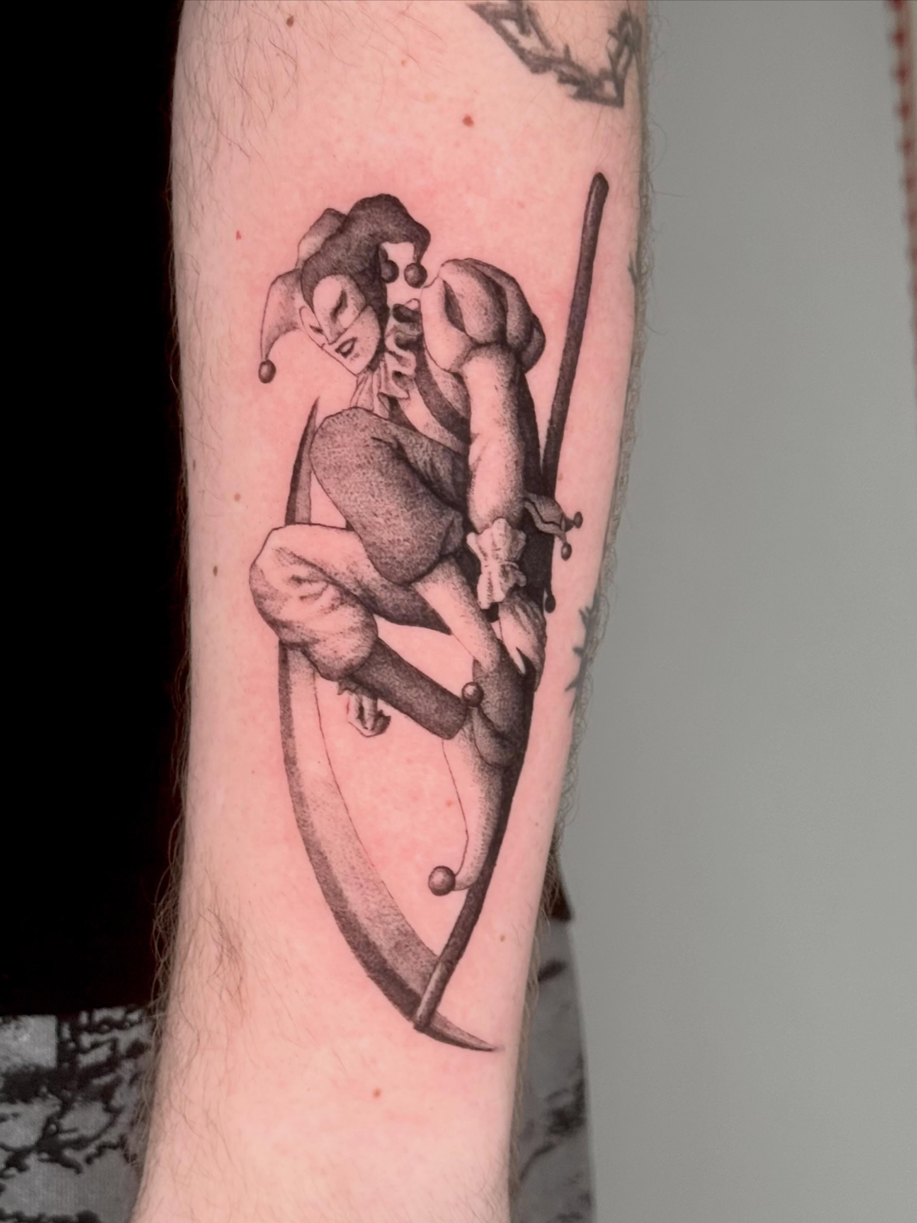 Jester and scythe black and grey tattoo on the forearm by Andrew Flatts