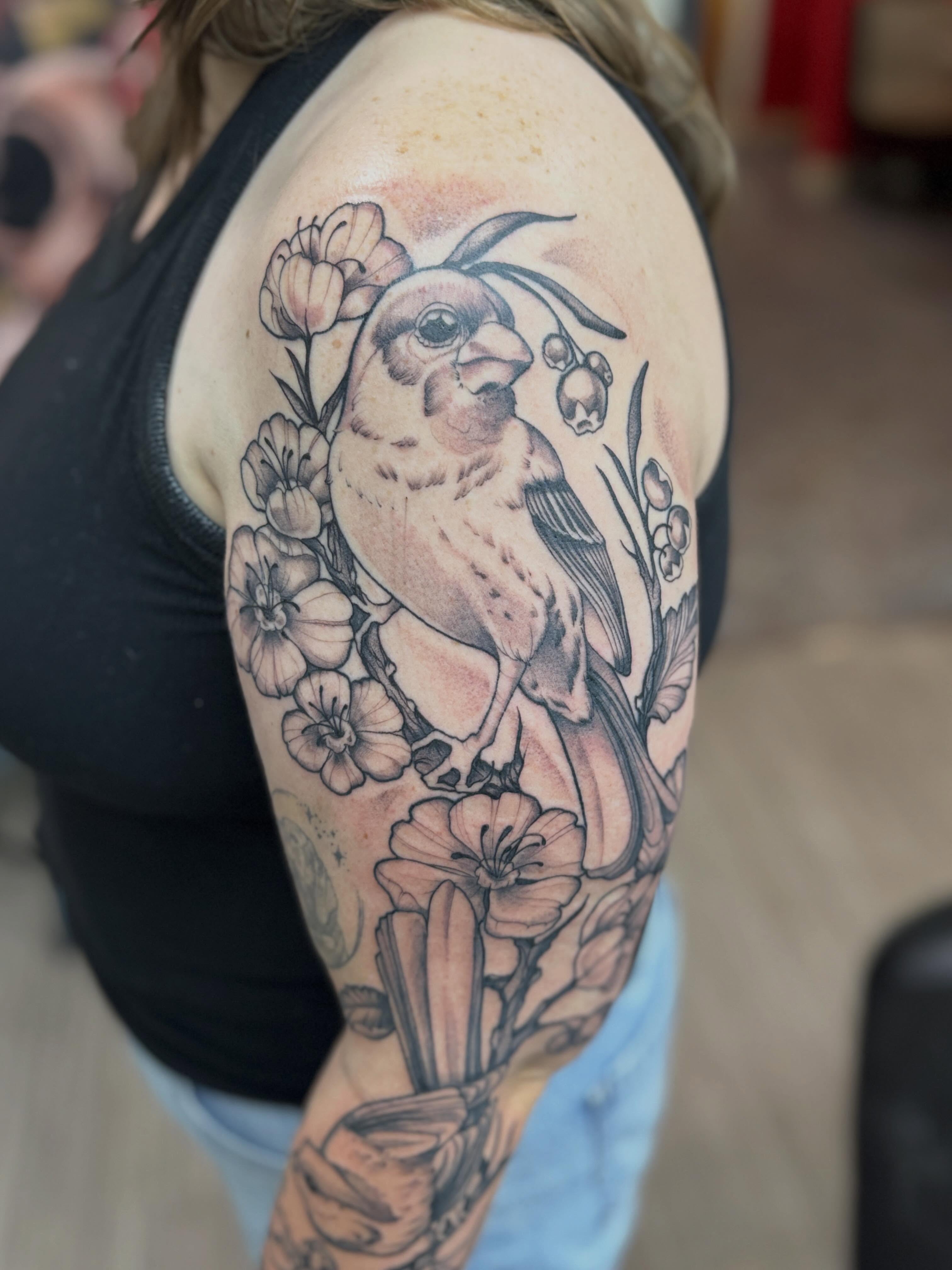 Bird and flowers realism tattoo on the upper arm by Rebecca Rose