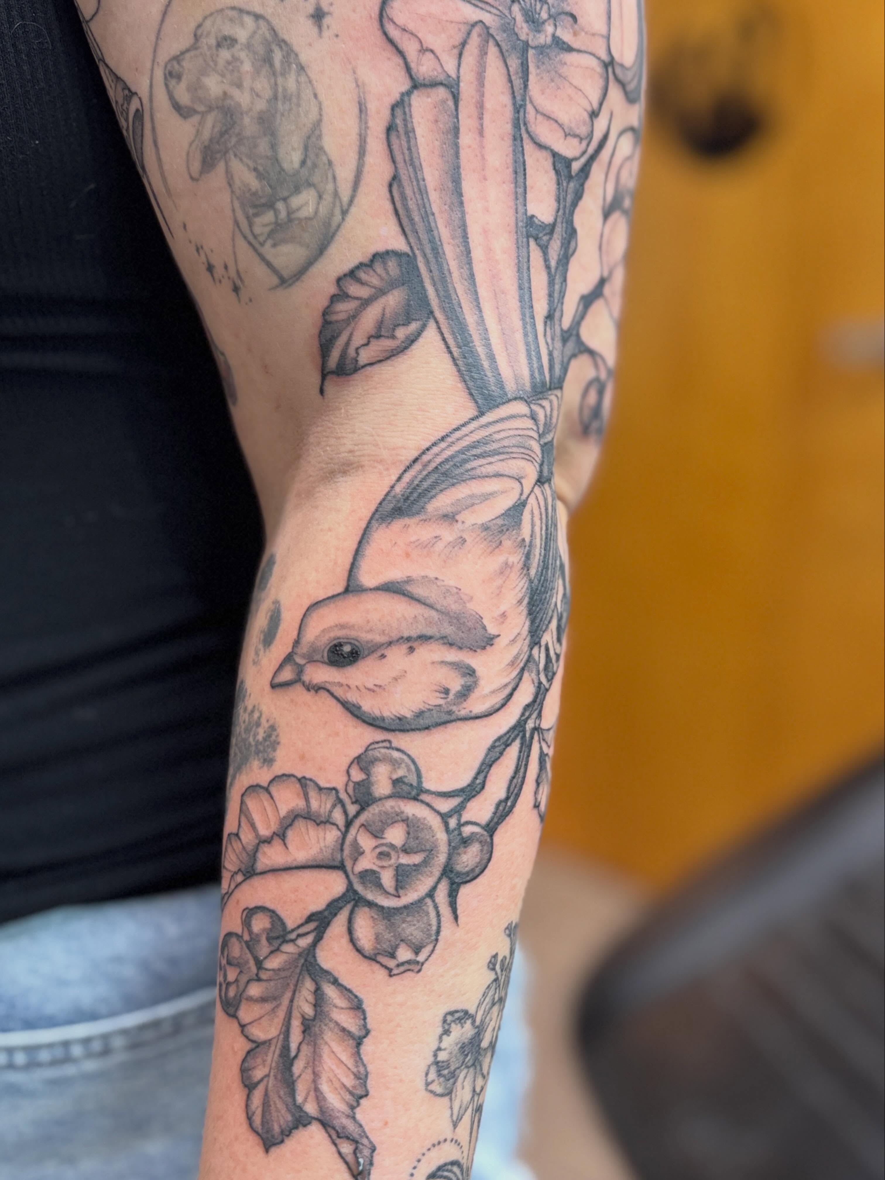 Bird and flowers black and grey tattoo on the forearm by Rebecca Rose