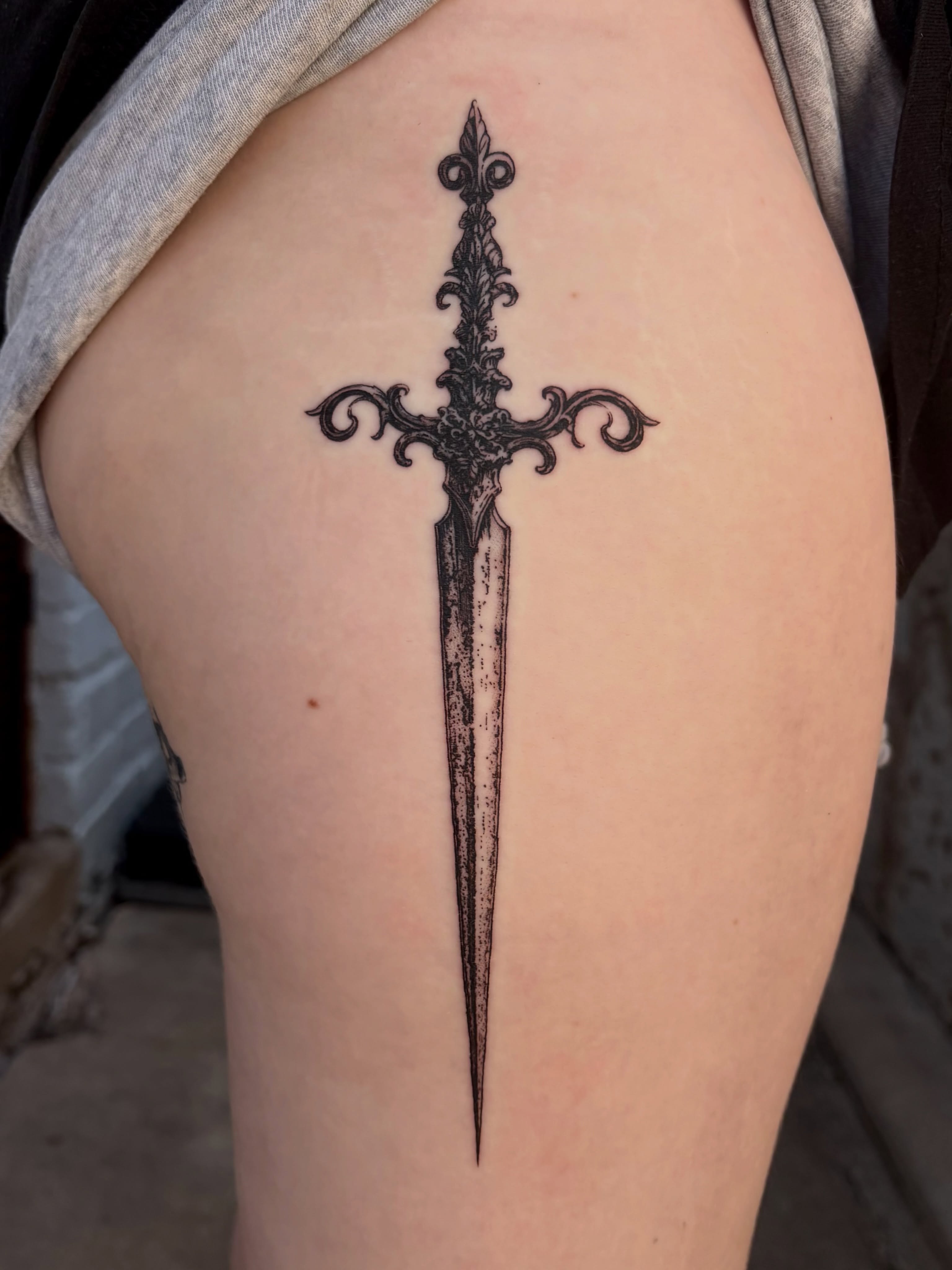 Sword black and grey tattoo on the thigh by Kylah Amin Tattoo