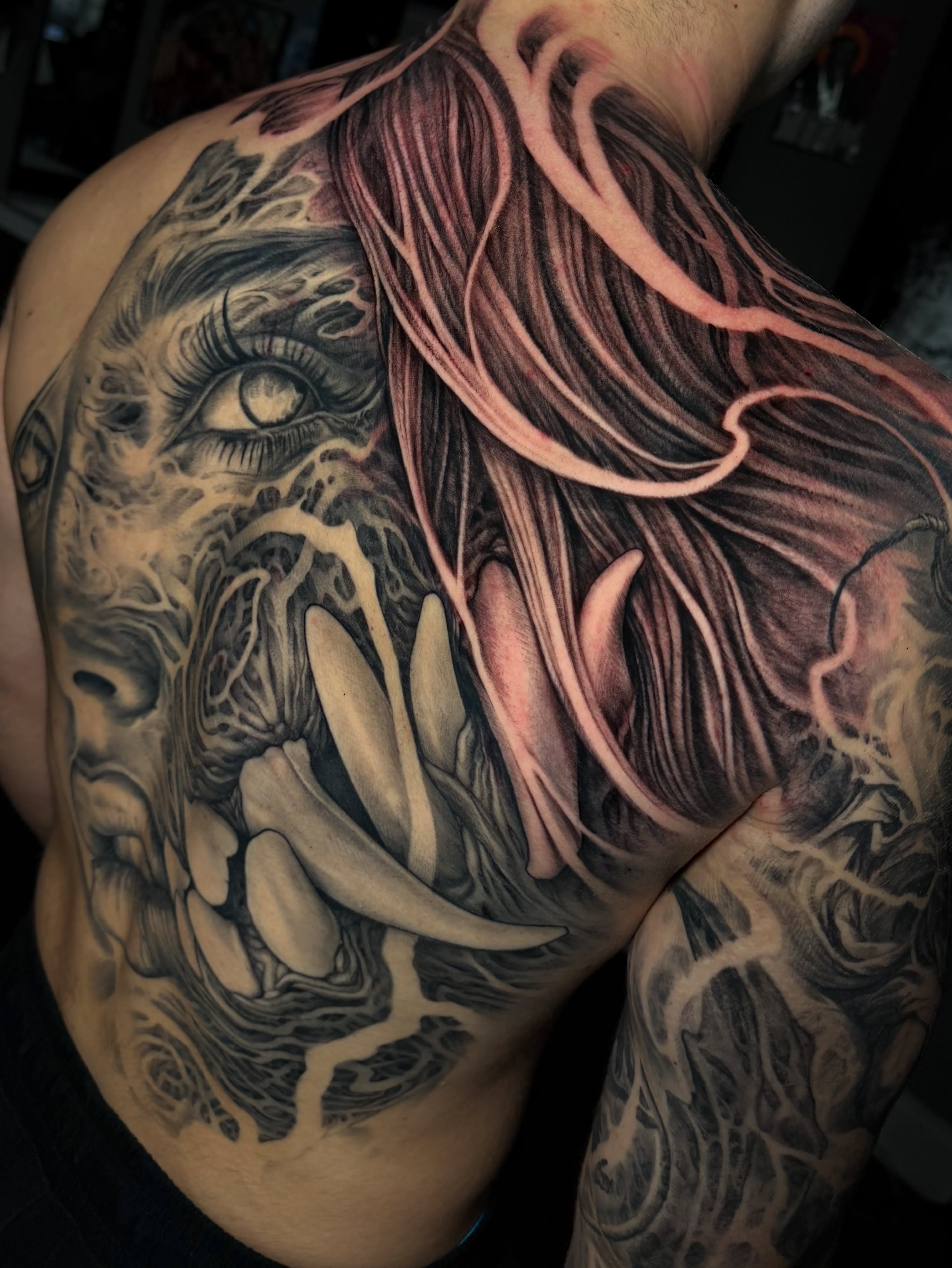 Monstrous face with flowing hair dark art tattoo on the shoulder by Nico Perez