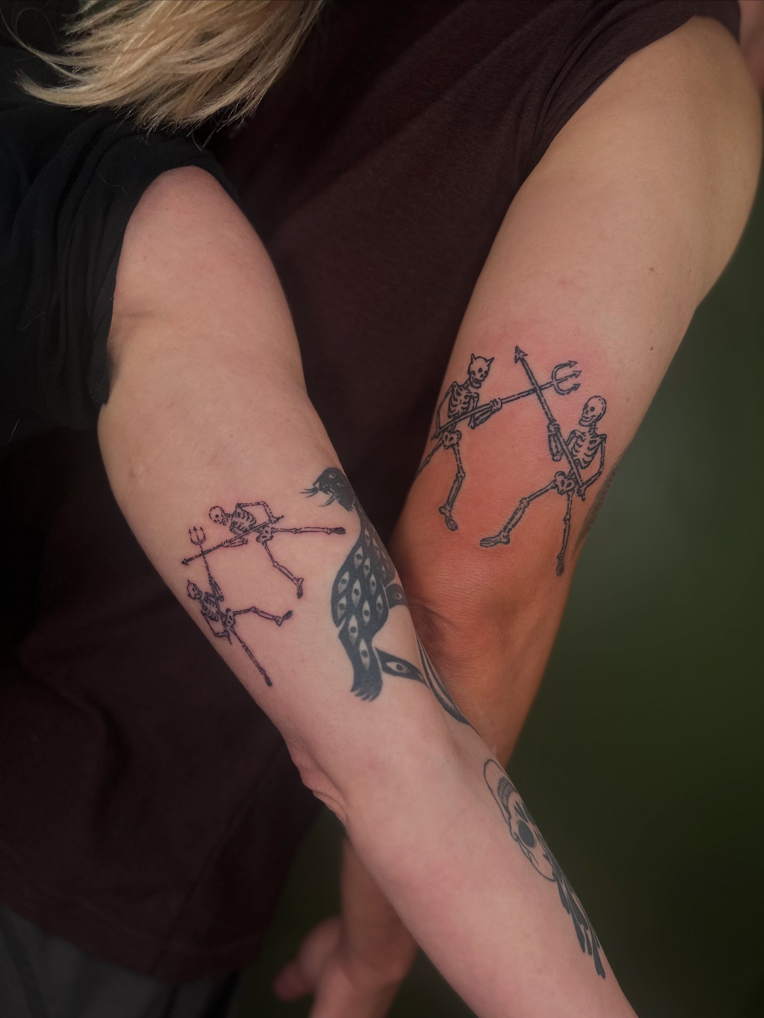 Skeletons dancing black and grey tattoo on the forearm by Nikolas Tapio Aatos Mäkelä
