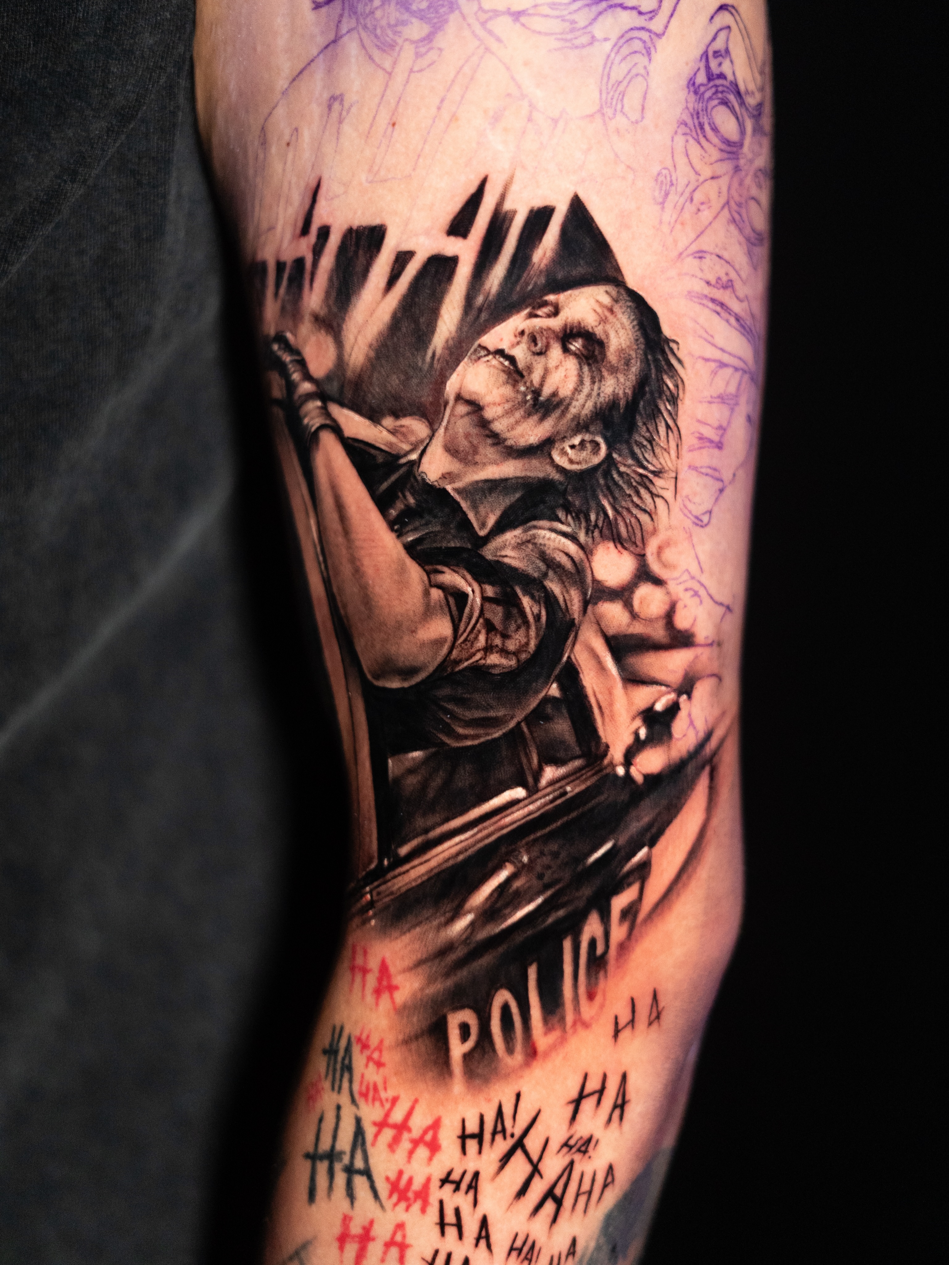 The Joker in a police car realism tattoo on the forearm by James Jurado