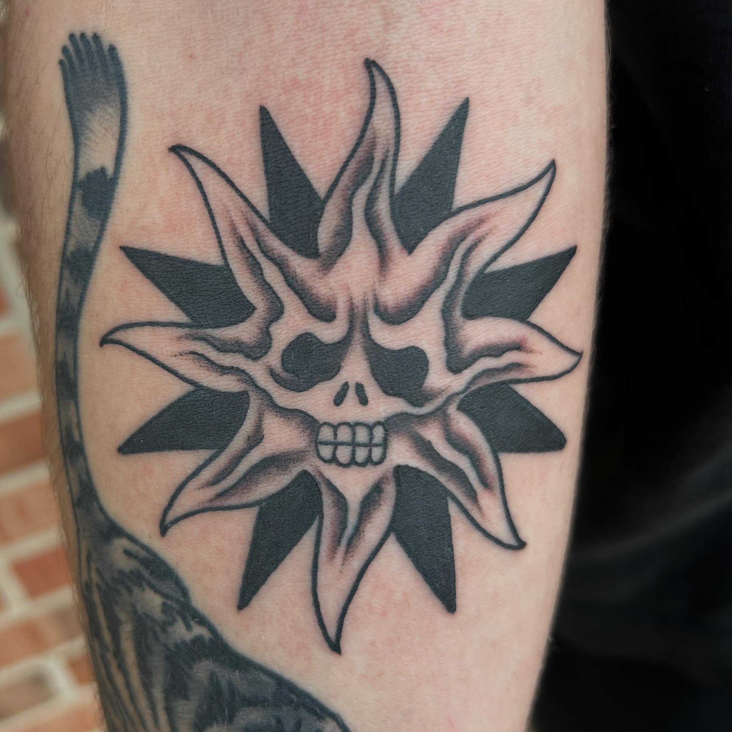 Skull with spiky crown black and grey tattoo on the forearm by Zach Andrews