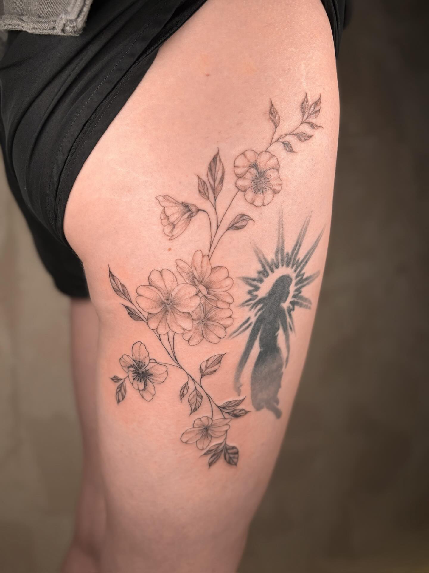 Flowers and silhouette black and grey tattoo on the thigh by Annie