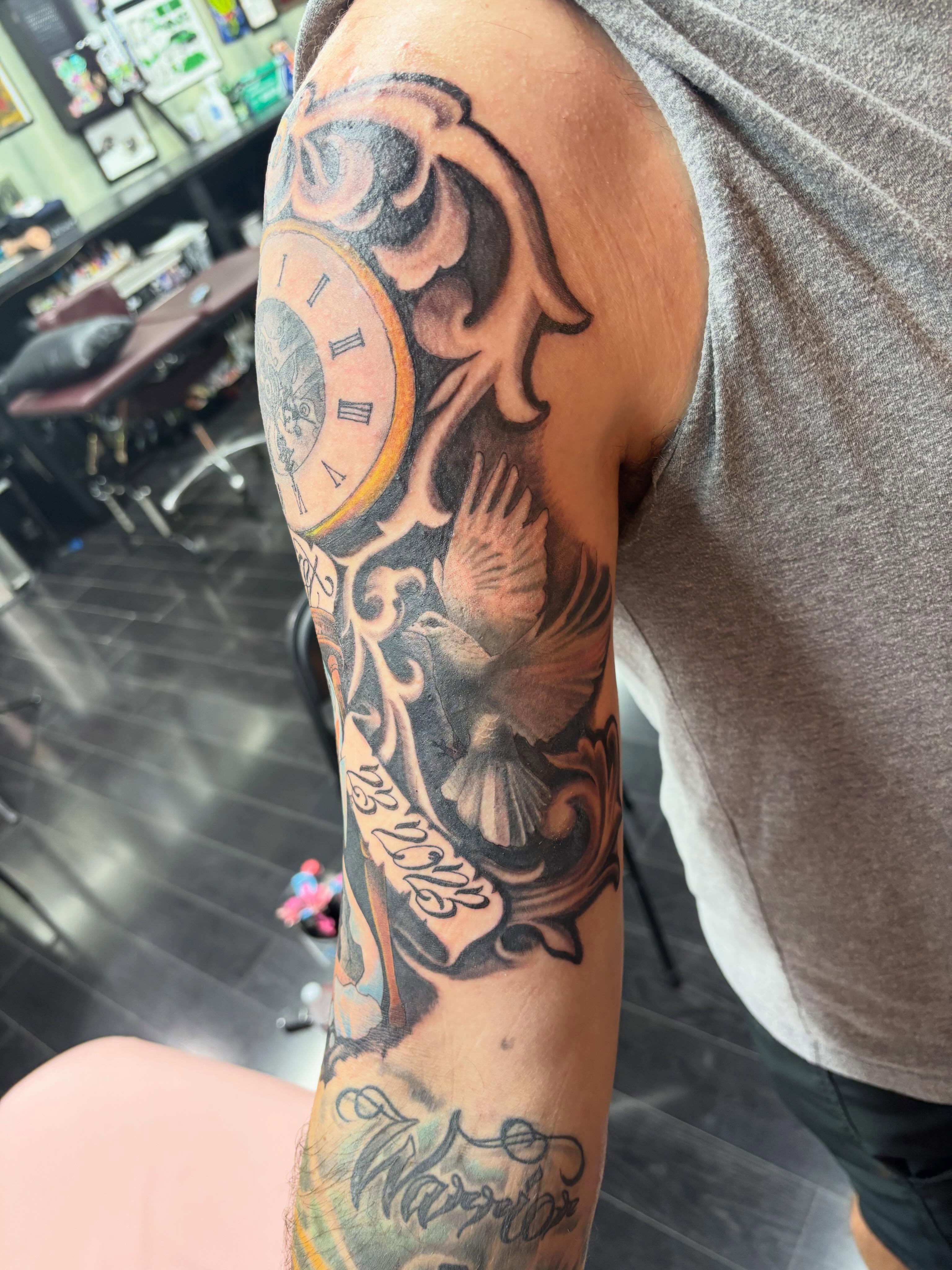 Clock and dove American traditional tattoo on the upper arm by Oscar Cuéllar (Kue-Yar)