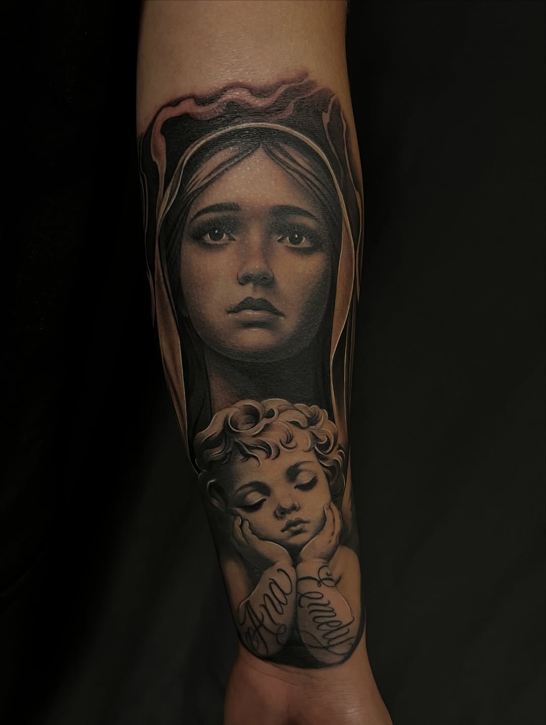 Virgin Mary and cherub with lettering Chicano tattoo on the forearm by Thomas Conard