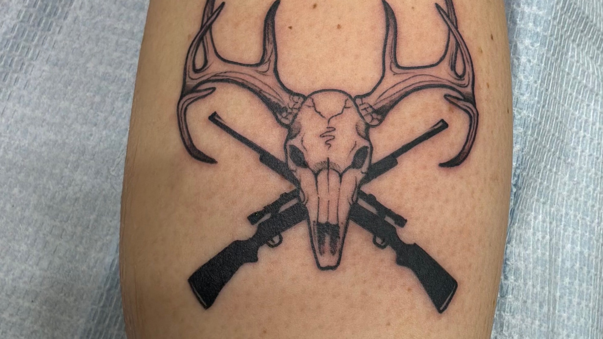 Deer skull and rifles black and grey tattoo on the forearm by German Romero-Rendon