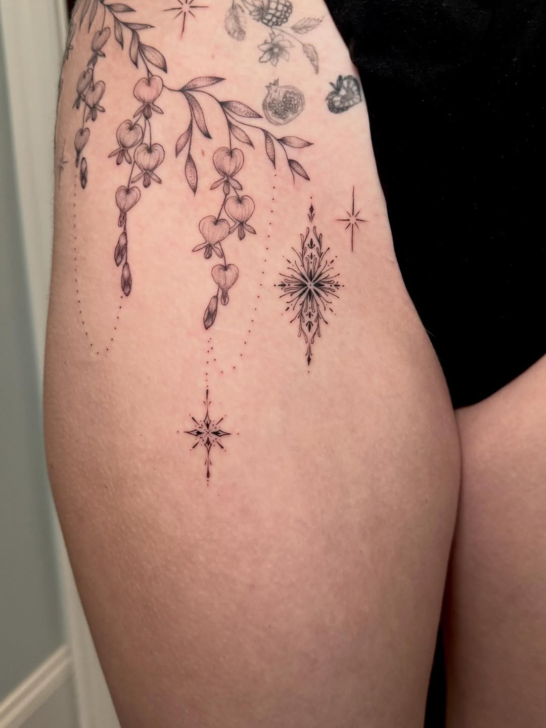 Bleeding hearts branch and stars ornamental tattoo on the thigh by Ana Blatt