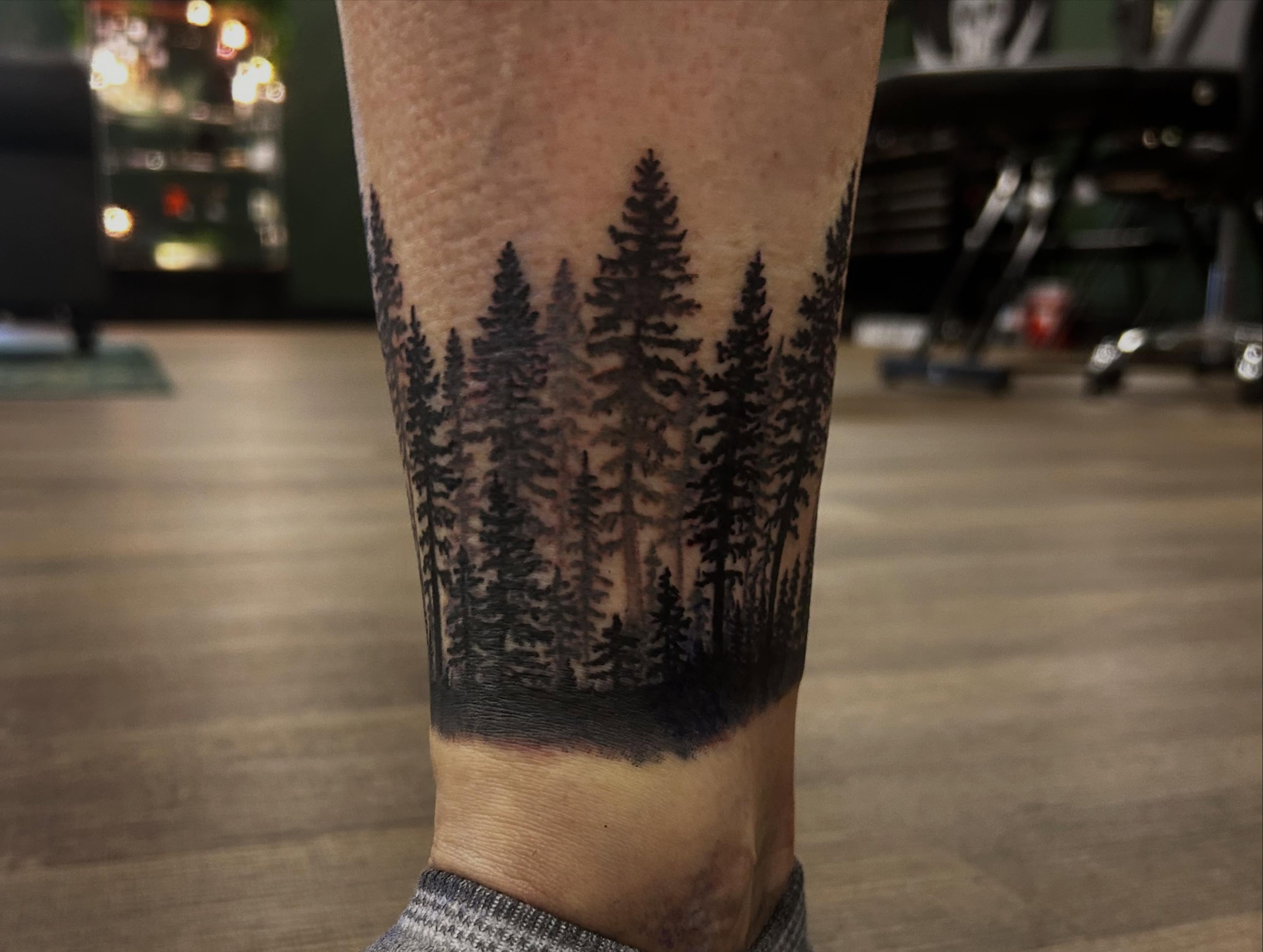 Pine trees black and grey tattoo on the forearm by Mayhem Andrews