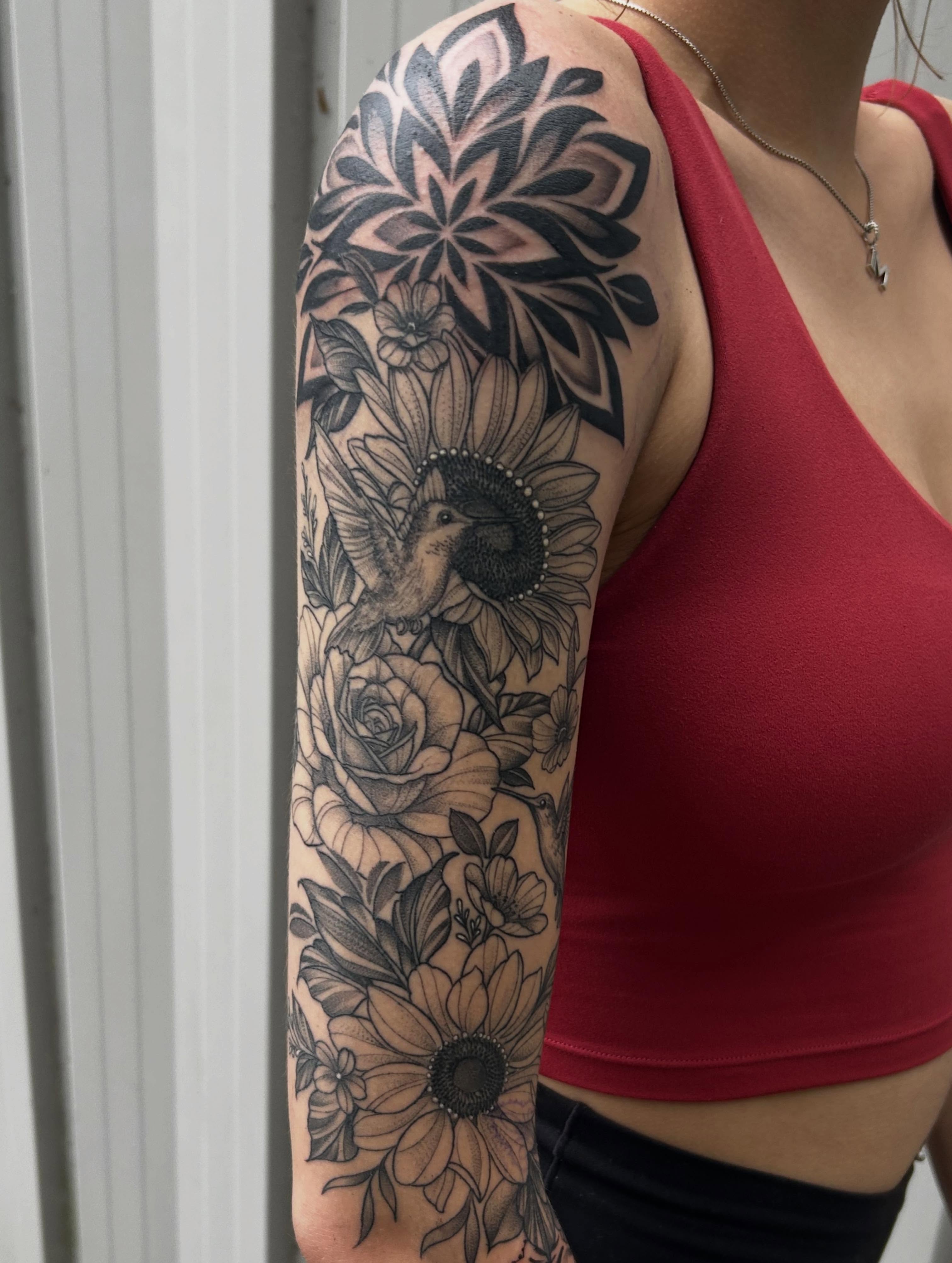 Floral and hummingbird realism tattoo on the upper arm by Mayhem Andrews