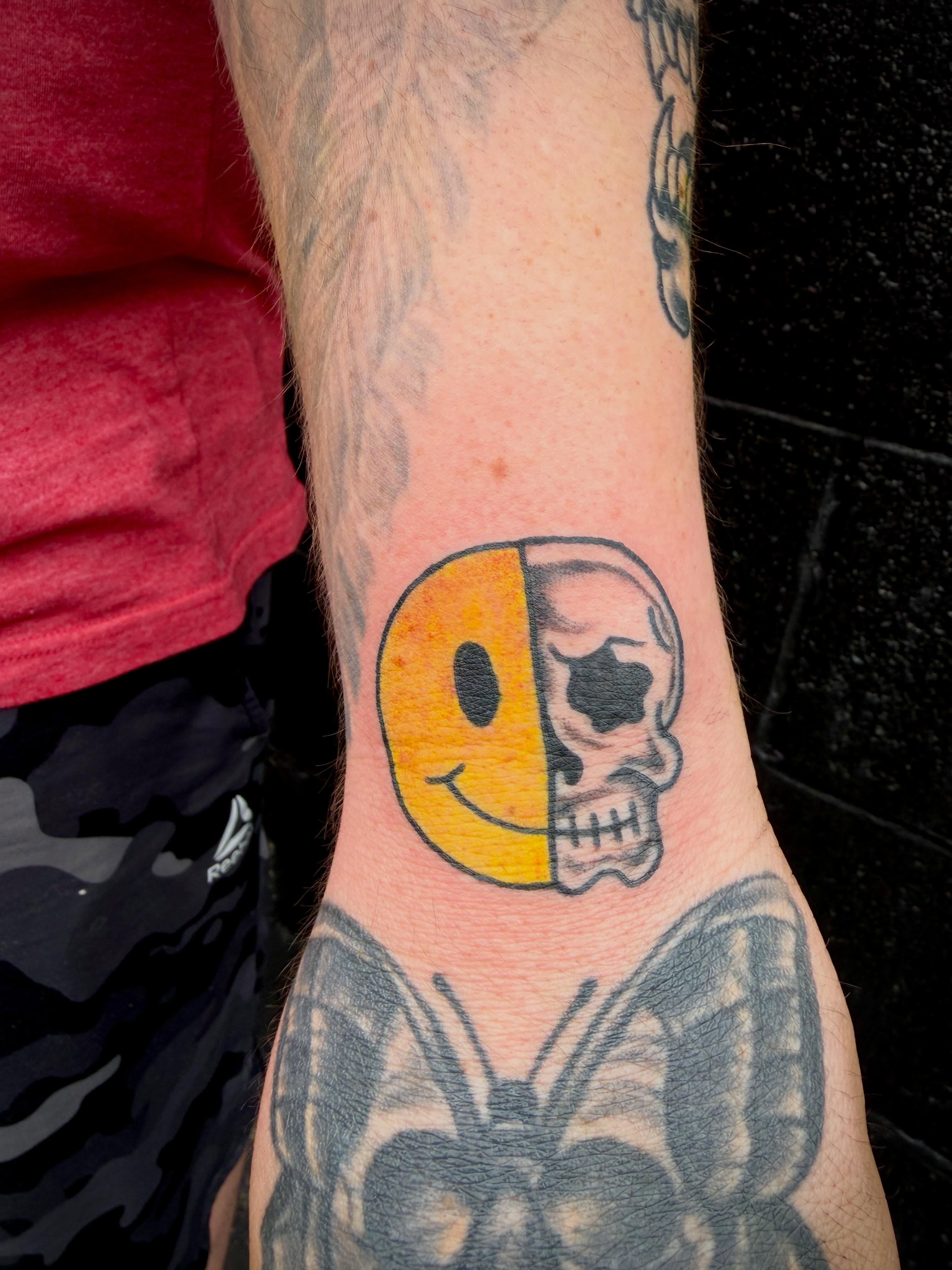 Smiley face and skull dotwork tattoo on the forearm by Ali Calis